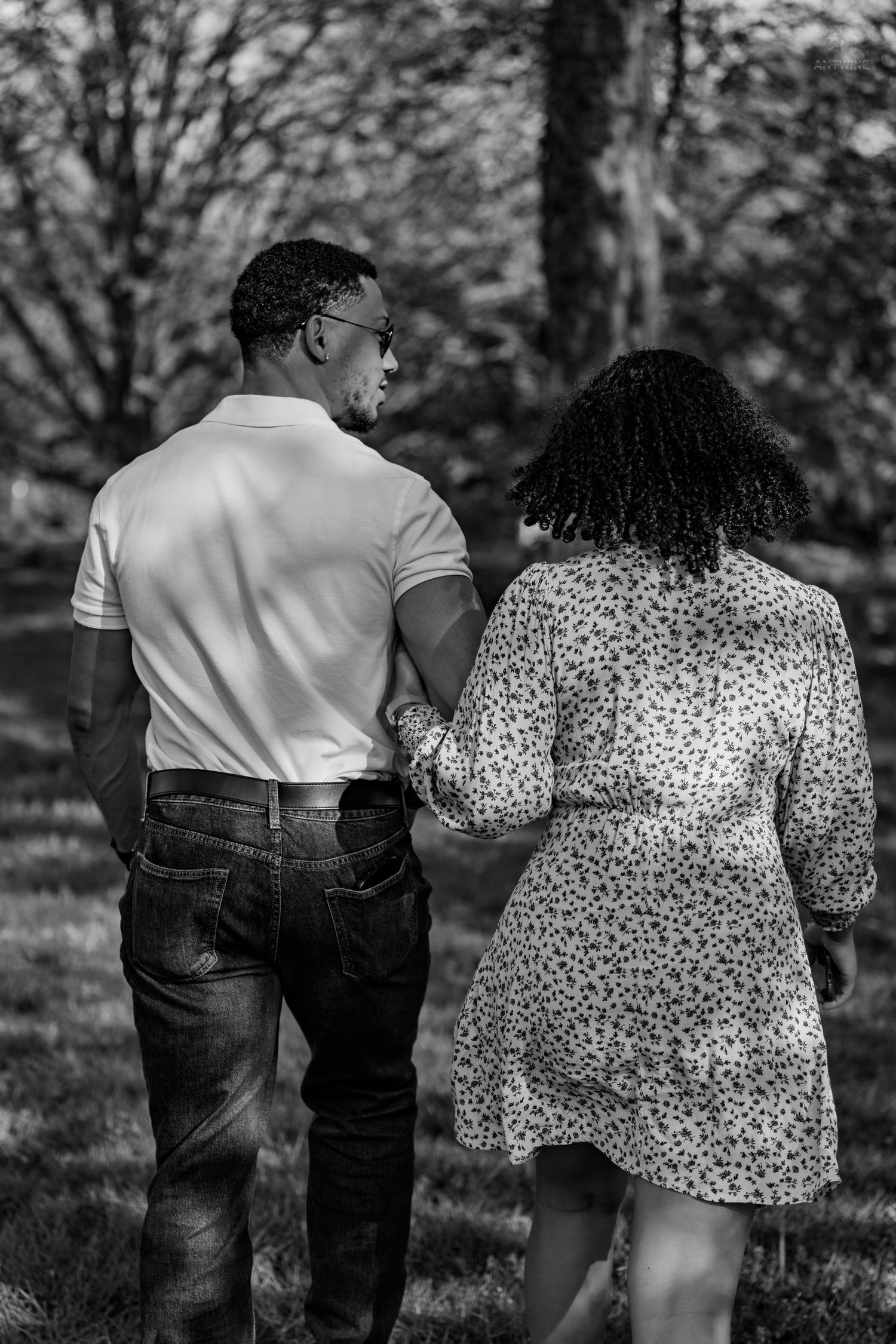 Couple walking hand in hand through a park, viewed from behind, black and white.