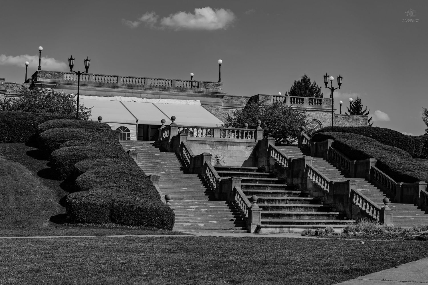 Black and white photo of elegant stone staircase with manicured hedges leading to a white event tent.