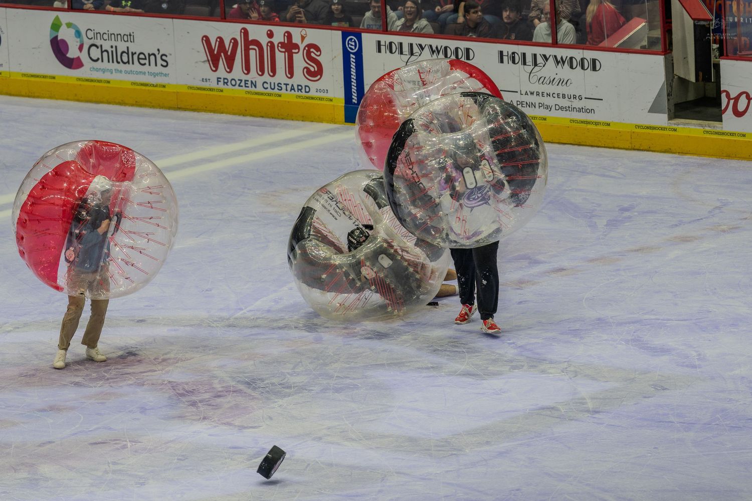 Participants in colorful bubble soccer balls colliding on an ice rink during a fun intermission game.