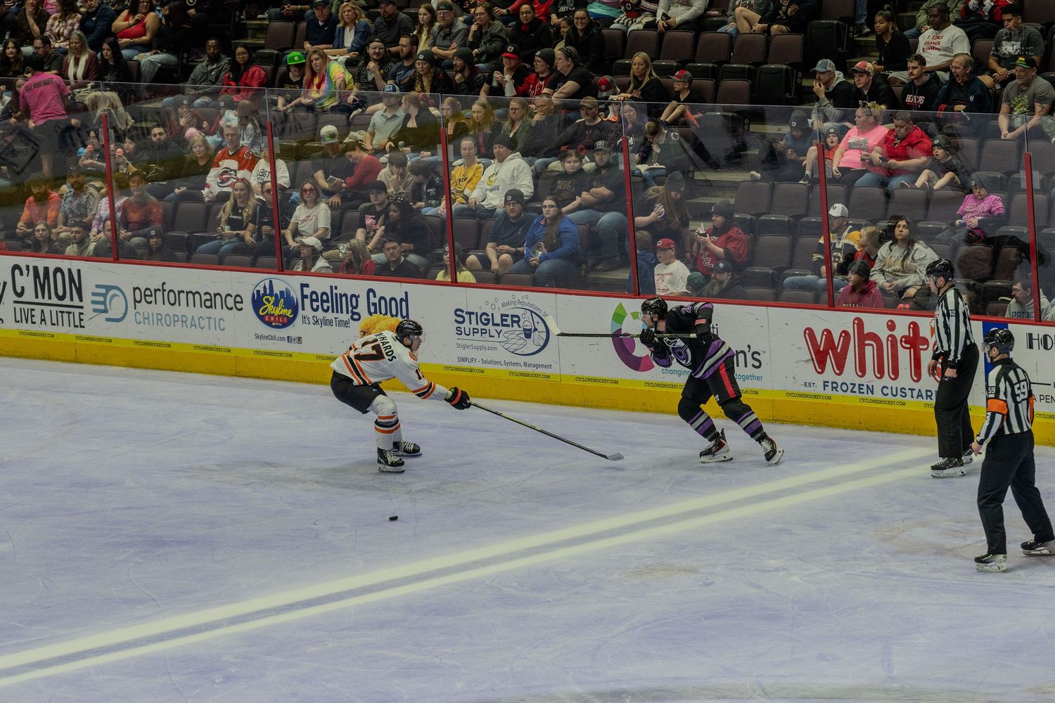 Two hockey players race for the puck along the boards during a competitive professional ice hockey game.