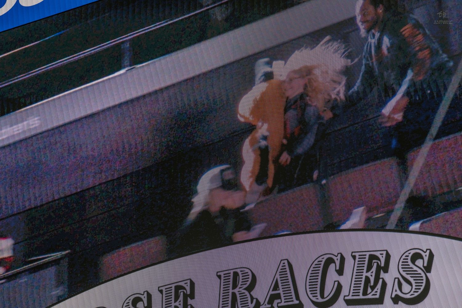 Excited fans celebrate during a horse races promotion shown on an arena jumbotron screen.