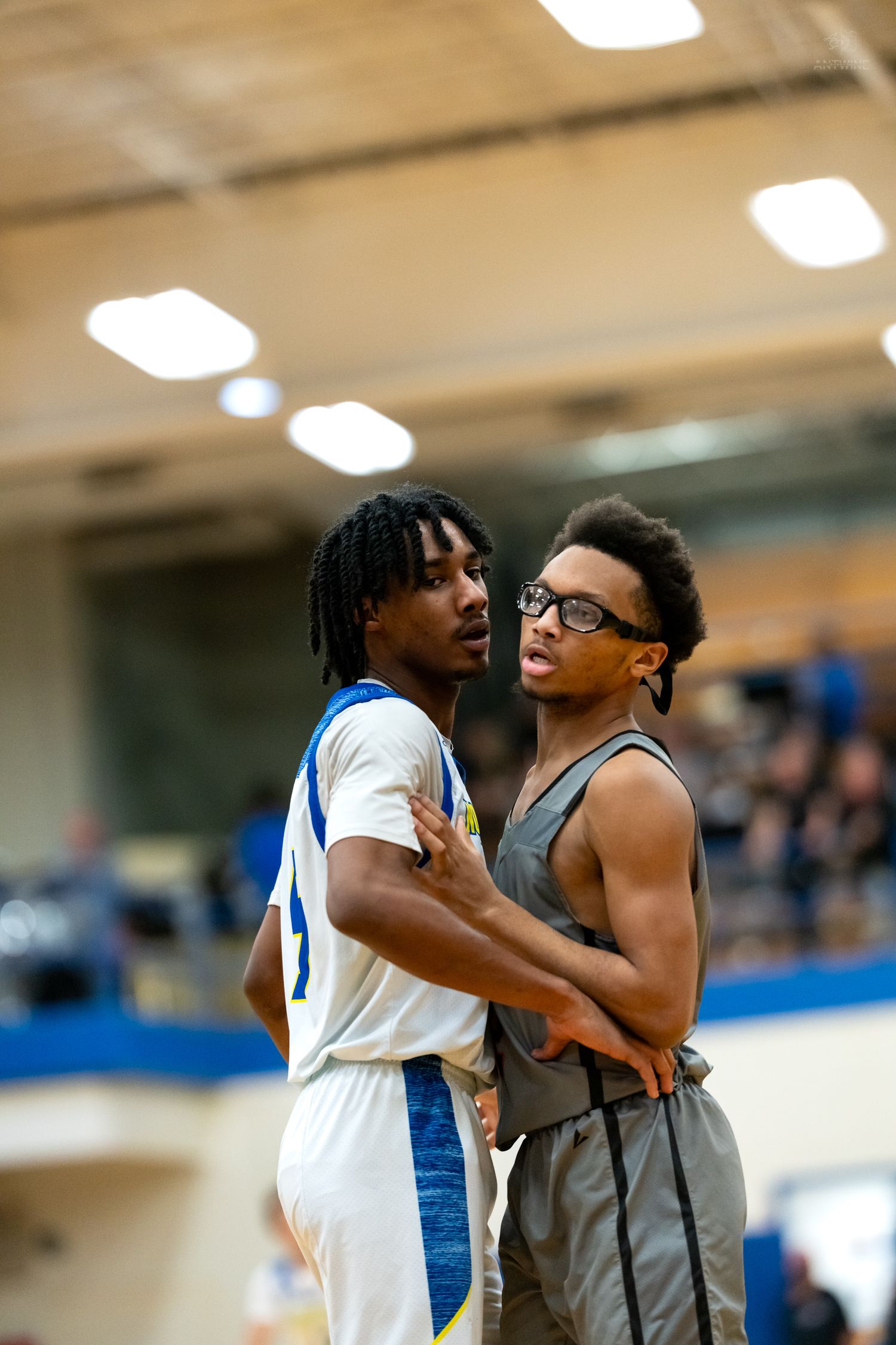 Two high school basketball players stand close together during timeout in indoor gymnasium game.