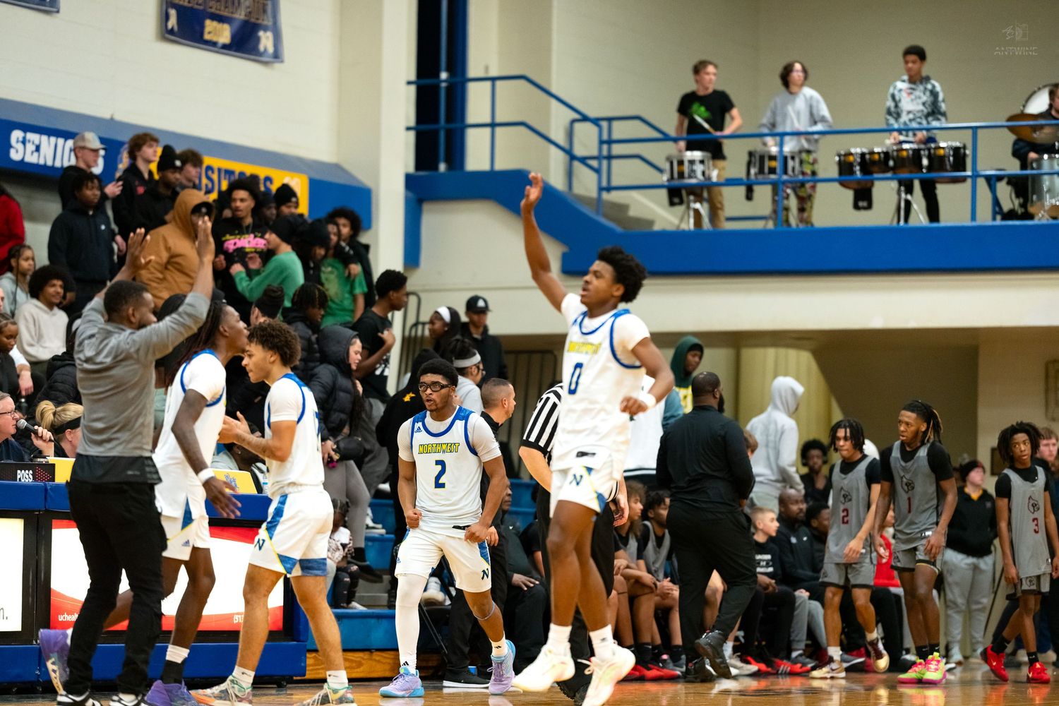 Basketball team erupts in celebration on the sideline during a high school gymnasium game.