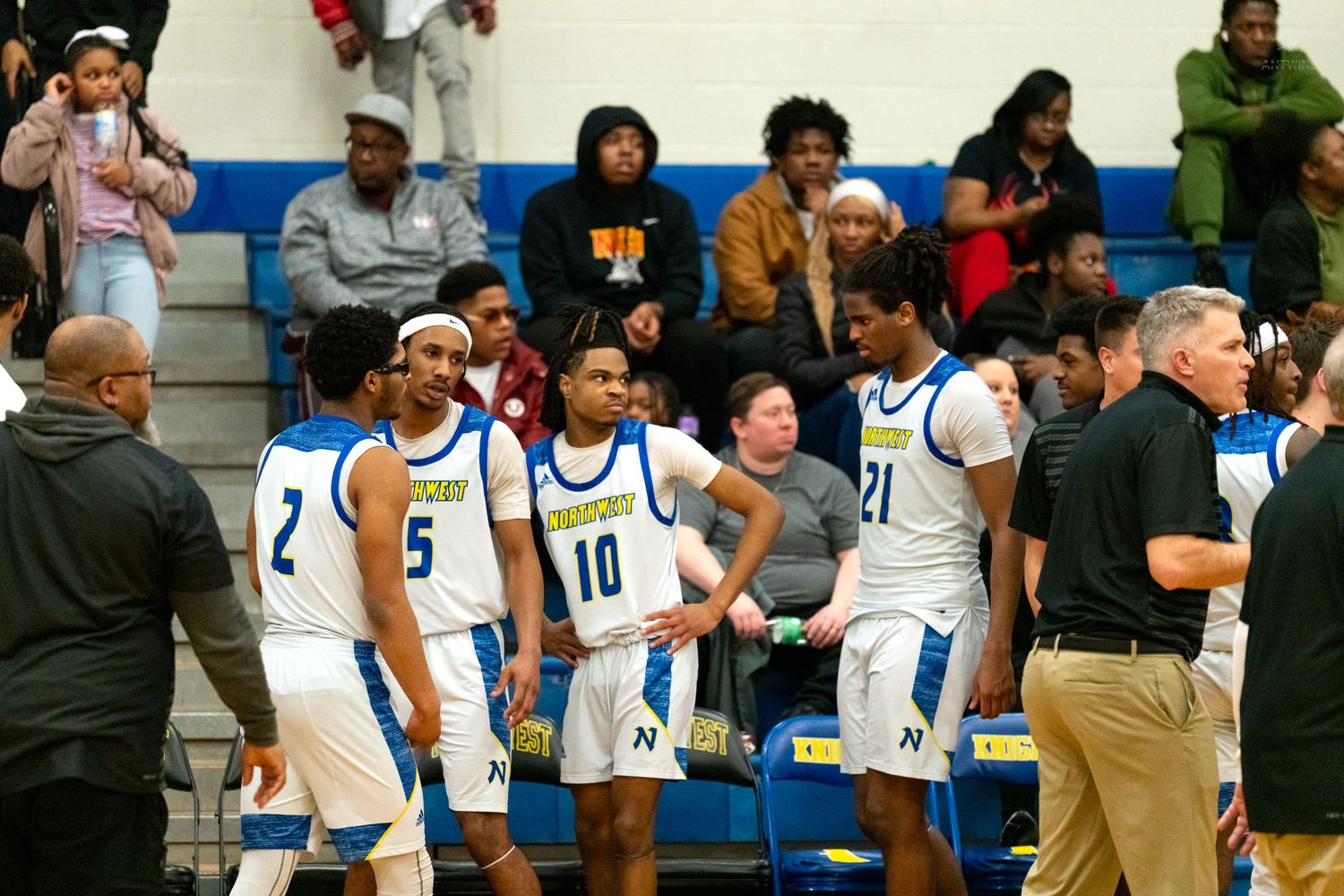 Northwest Knights basketball team huddles with coaches during a timeout in their blue and white uniforms.
