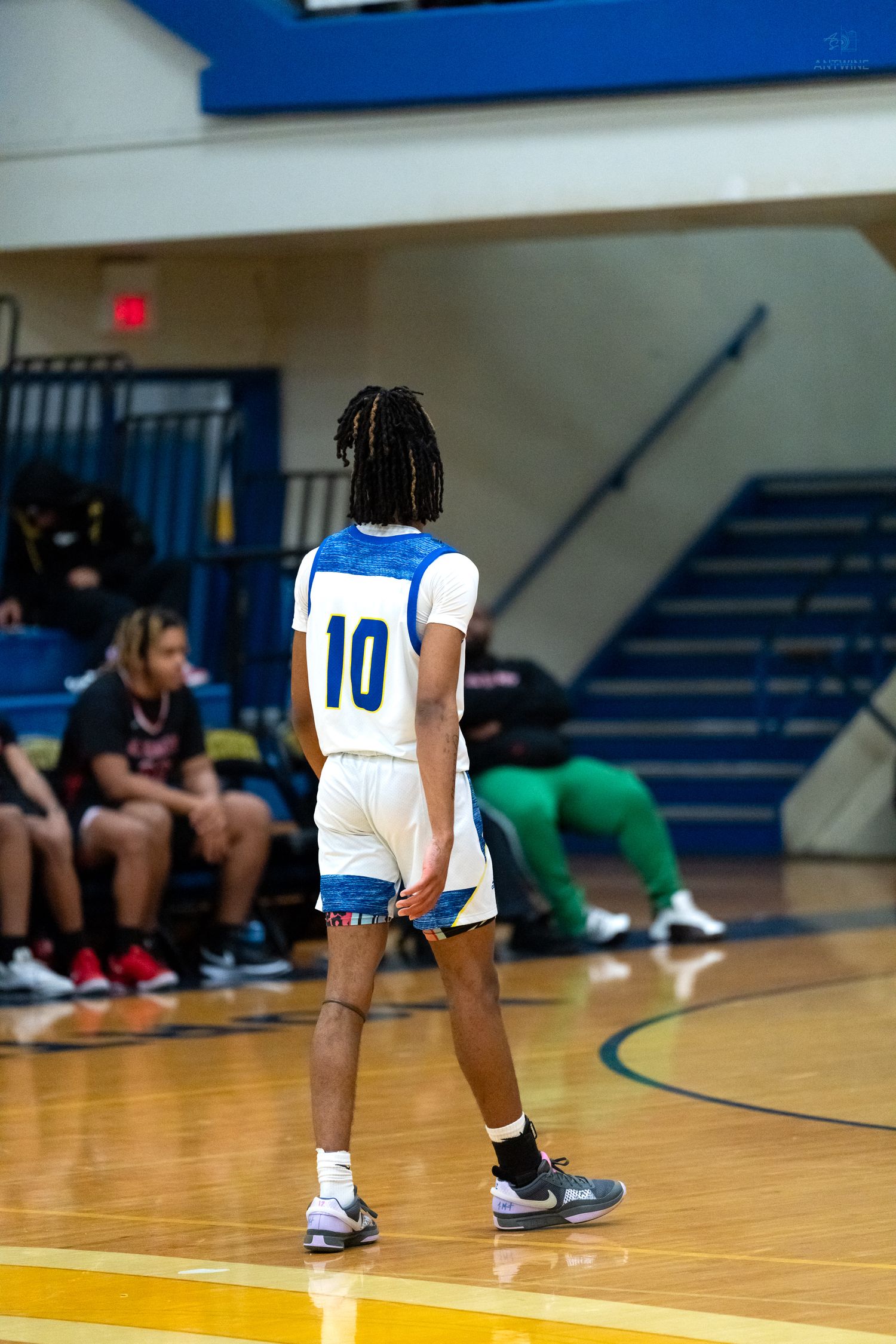 High school basketball player #10 in blue and white uniform stands on hardwood court.