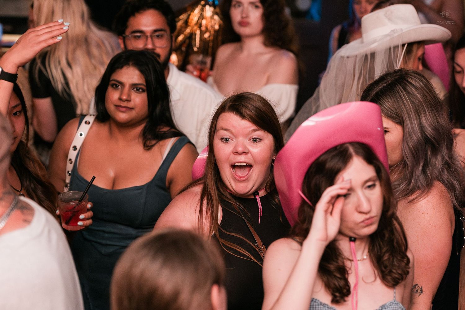 Excited group of women at a party, one wearing a pink cowboy hat in a nightclub.