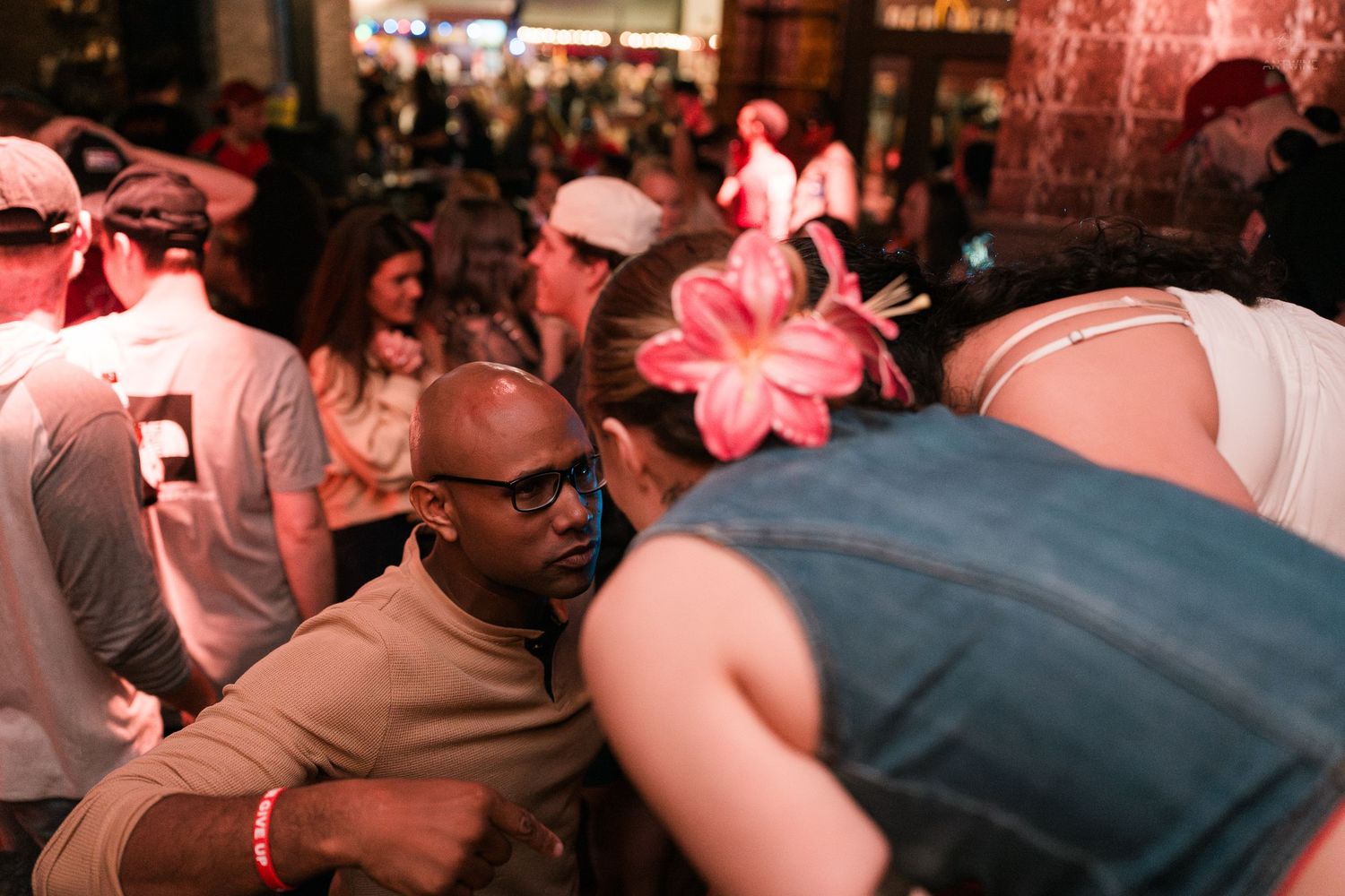 Bald man with glasses dancing with a woman wearing a pink flower at a nightclub.