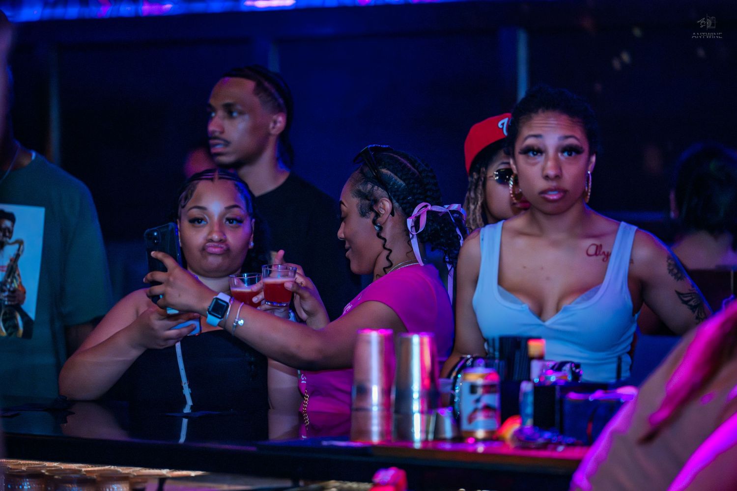 Women enjoying drinks together under purple neon lights at a bar.