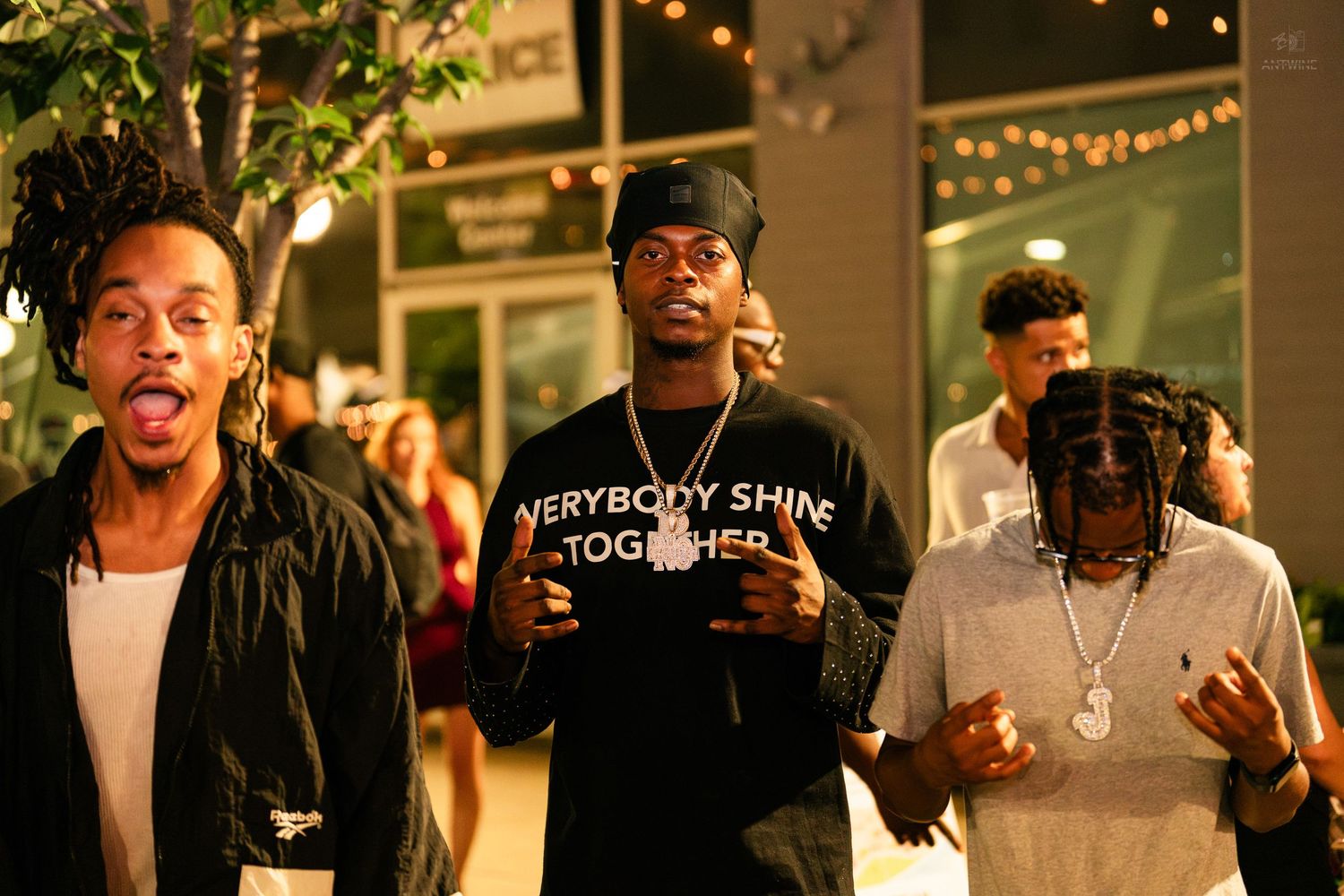 Group of young men walking outdoors at night, one wearing Everybody Shine Together shirt.