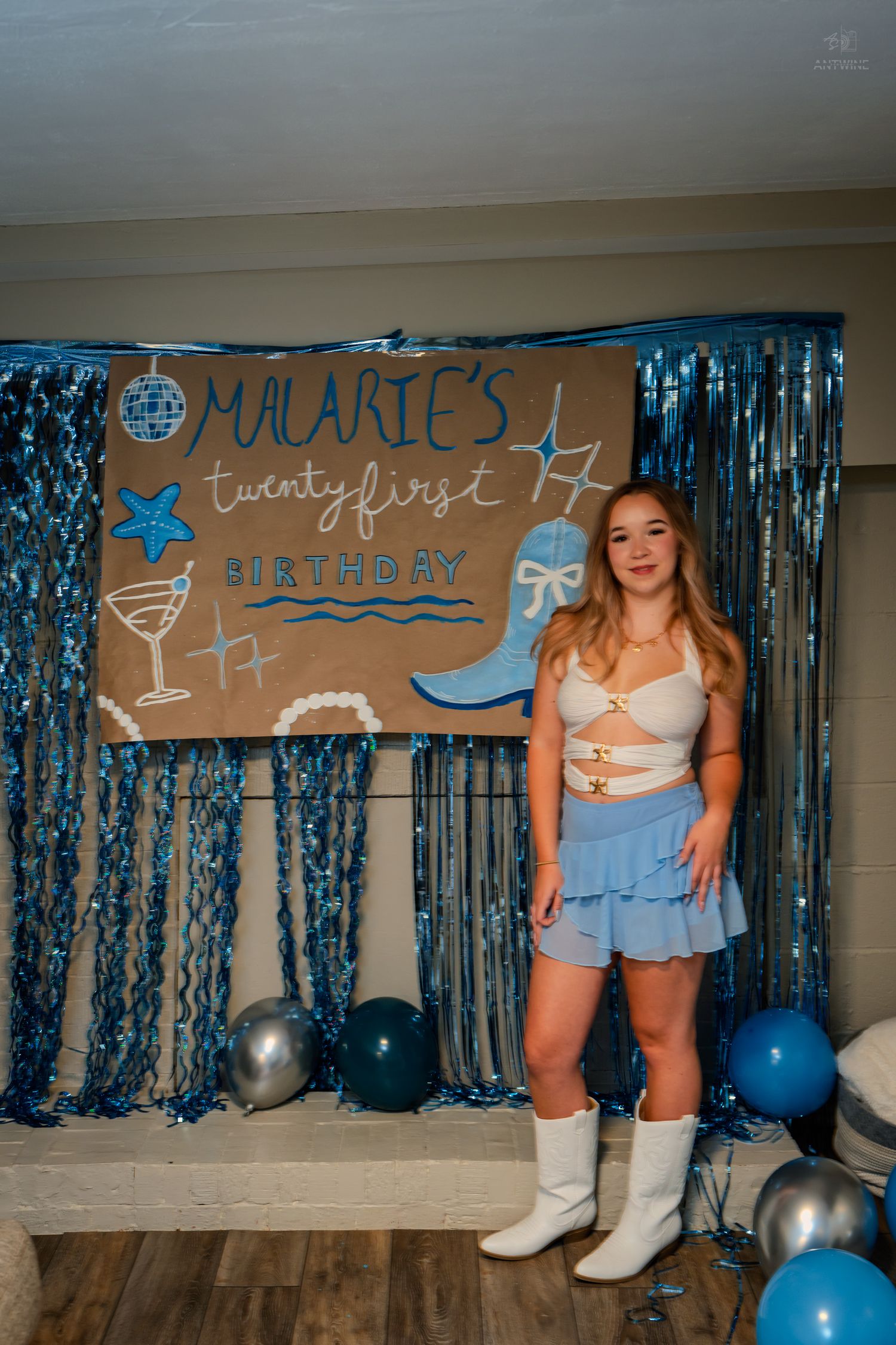 Woman in white cowboy boots and blue skirt smiling at Malarie's 21st birthday party decoration setup.