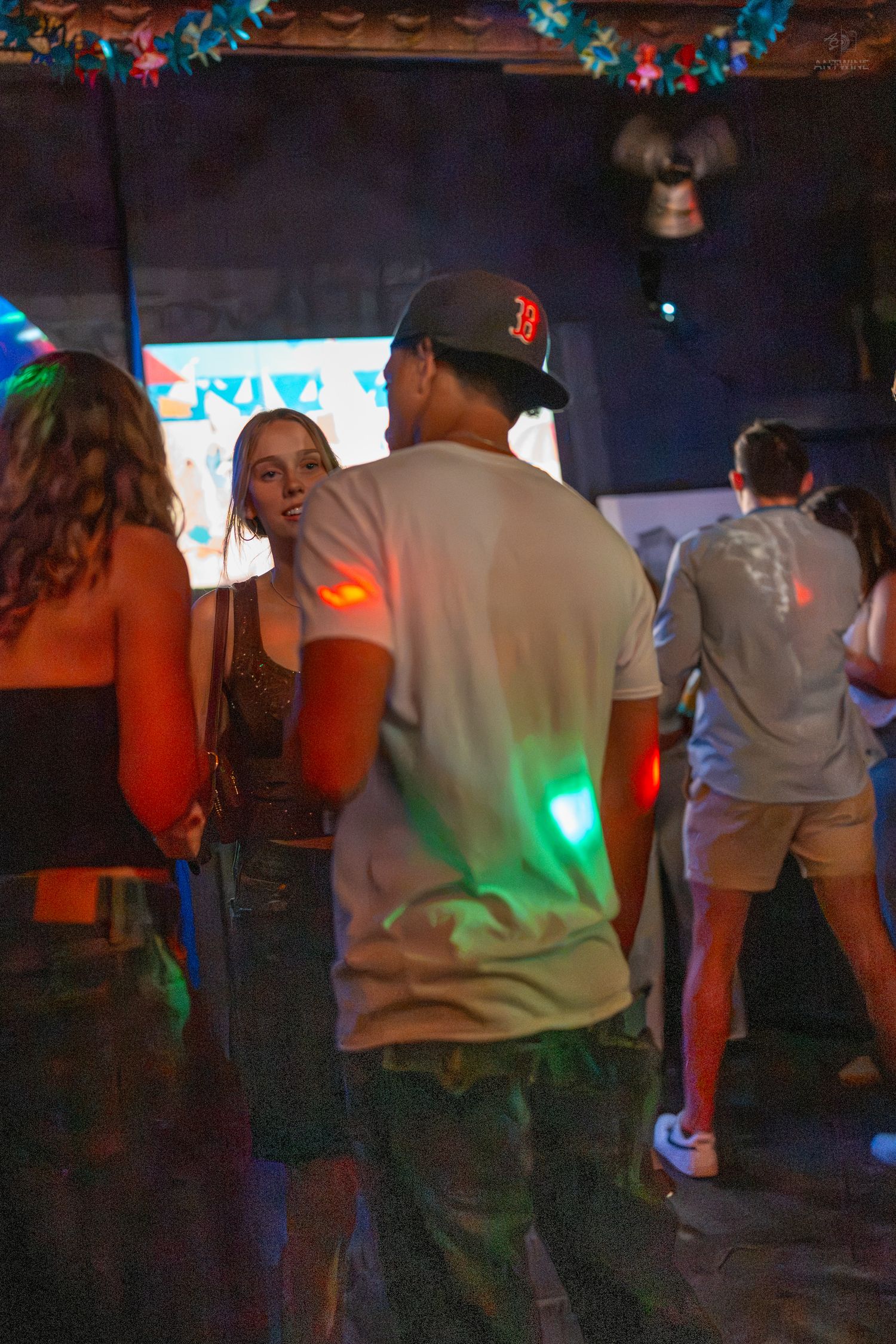 Young people dancing in a dimly lit nightclub with colorful green and red lights on the dance floor.