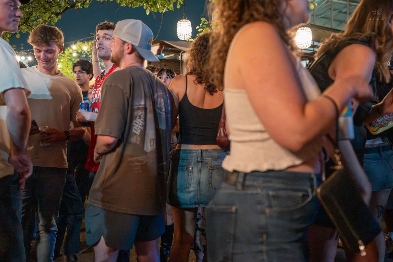 Crowd of young adults socializing at an outdoor nighttime festival or bar event.