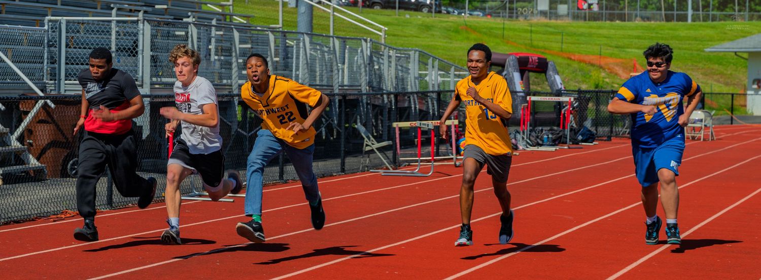 Students race on a red outdoor track during a school sports day event, with bleachers visible in the background.