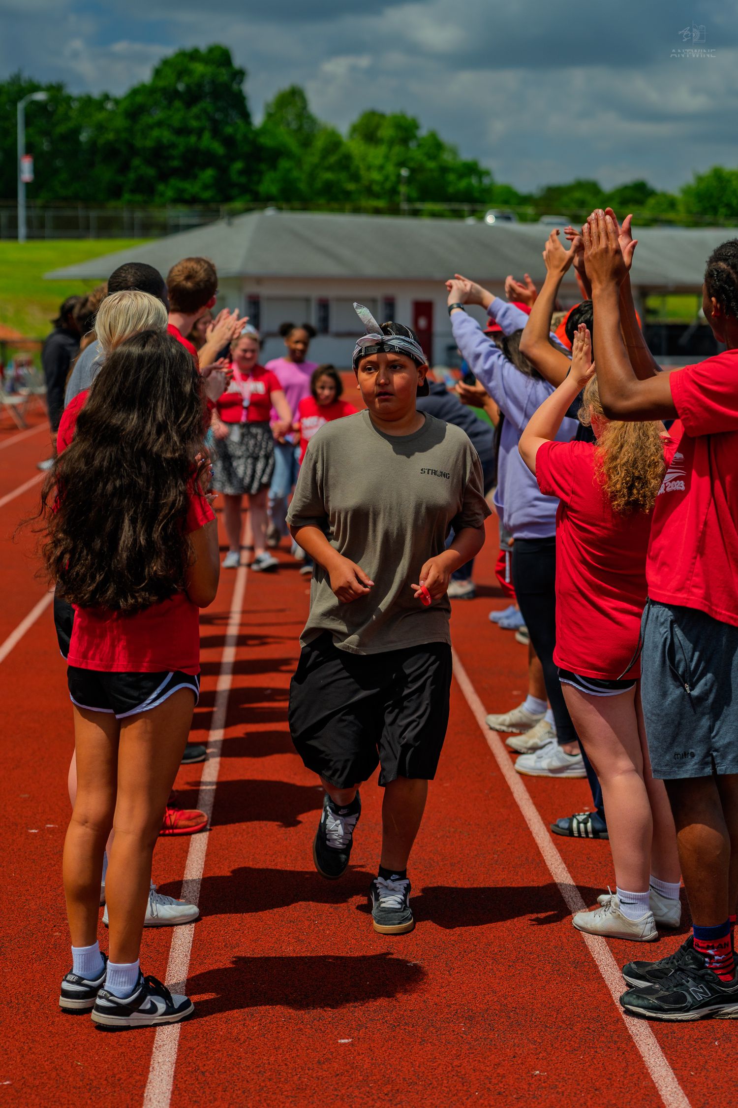 Student runs through a celebratory high-five tunnel on a red track during an outdoor school field day event.