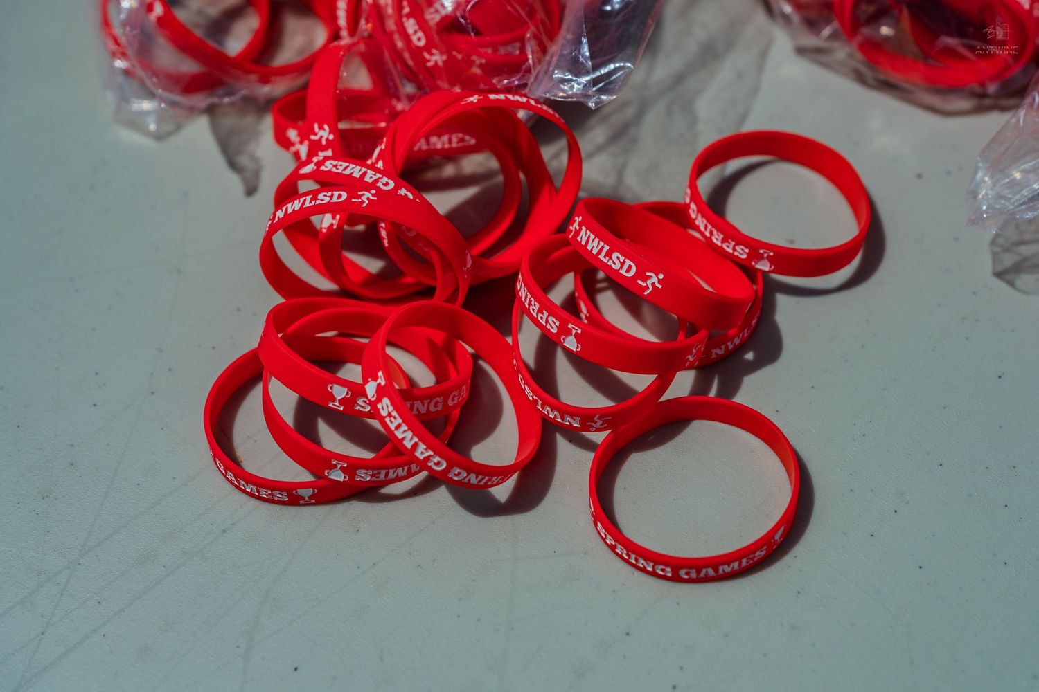 A pile of red silicone wristbands with white text on a light blue surface.