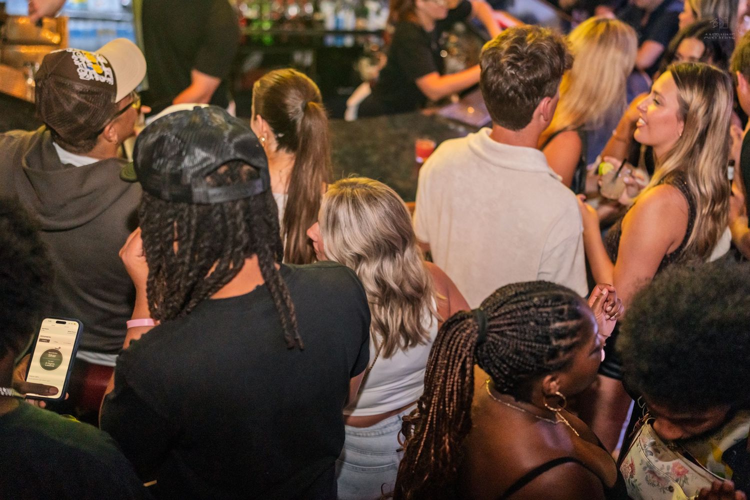Mixed group of friends gathered at a busy bar counter during a nightlife event.