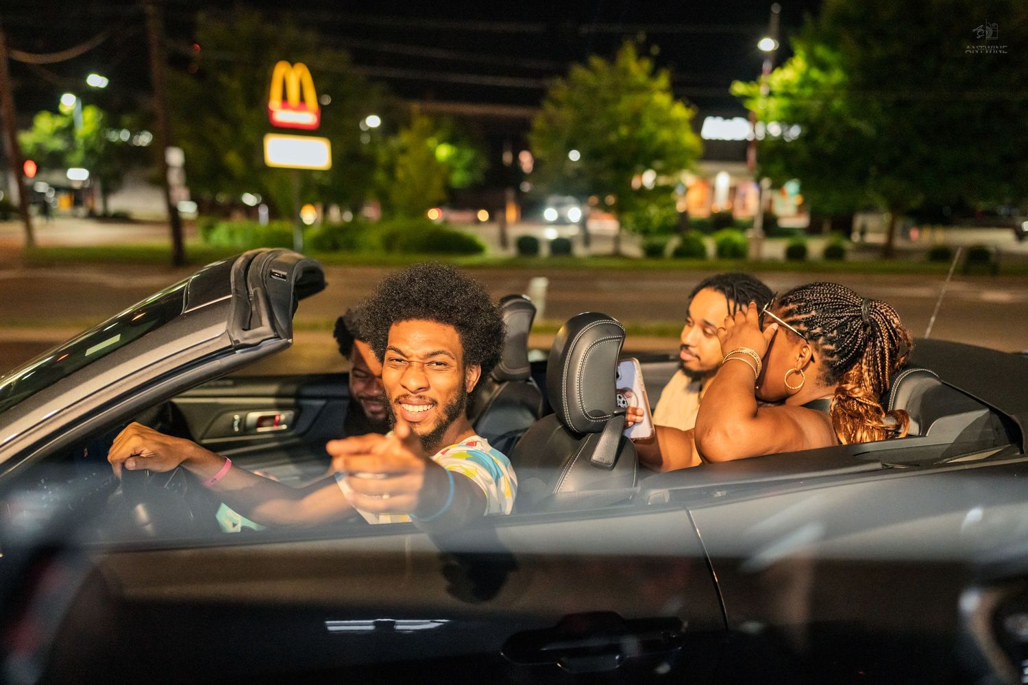 Three friends smiling in a convertible car at night near a McDonald's drive-thru.