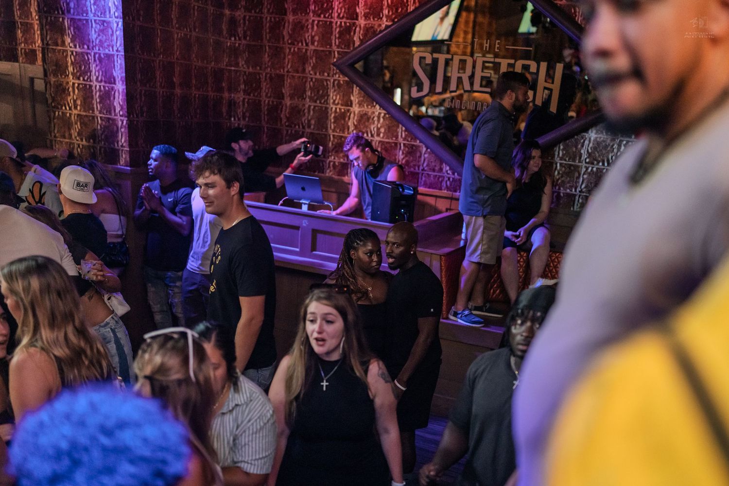 Excited crowd dances and socializes beneath Stretch nightclub sign during vibrant party.