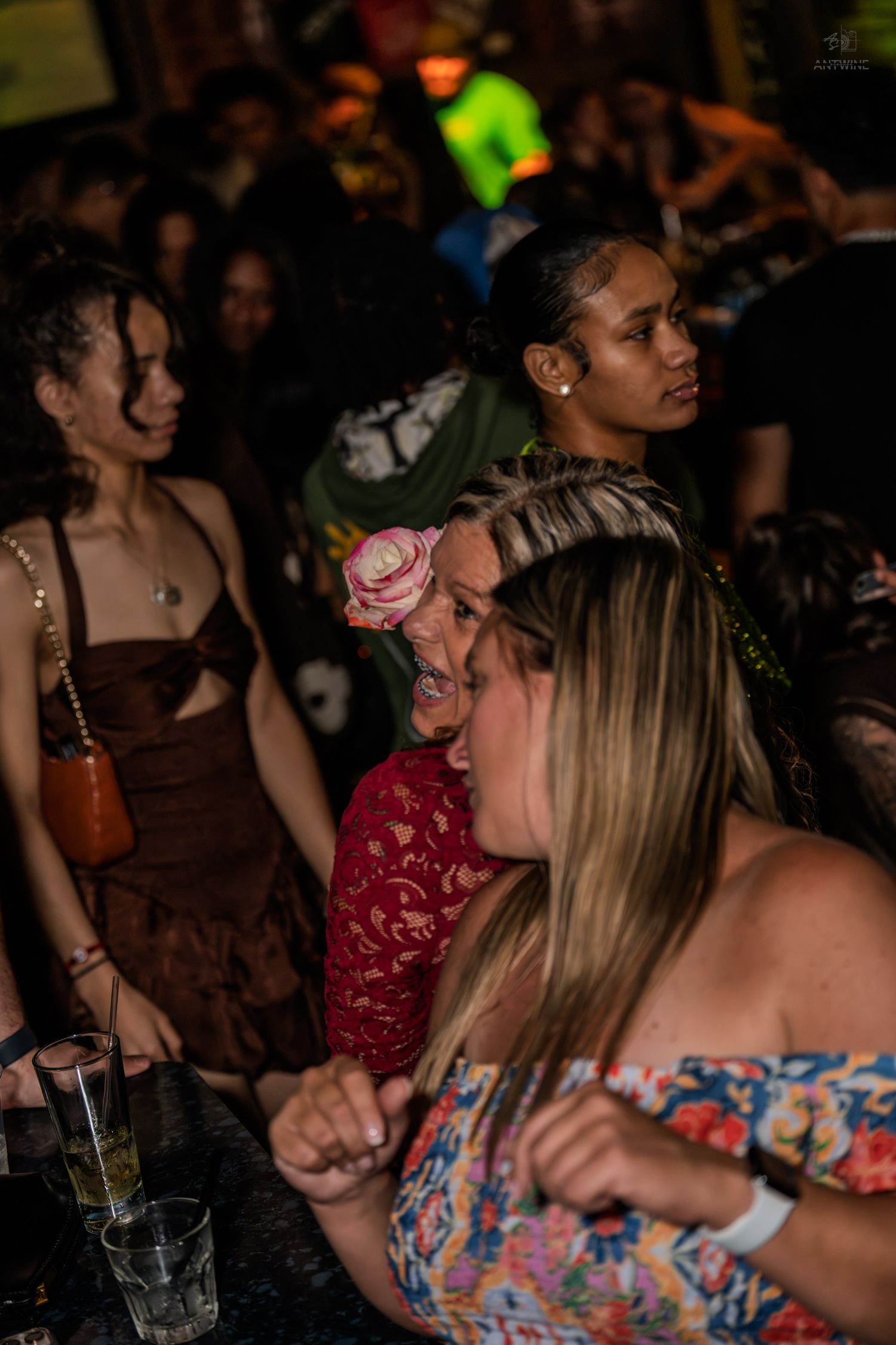 Women laughing and socializing at a lively nightclub bar with colorful lighting and crowd.