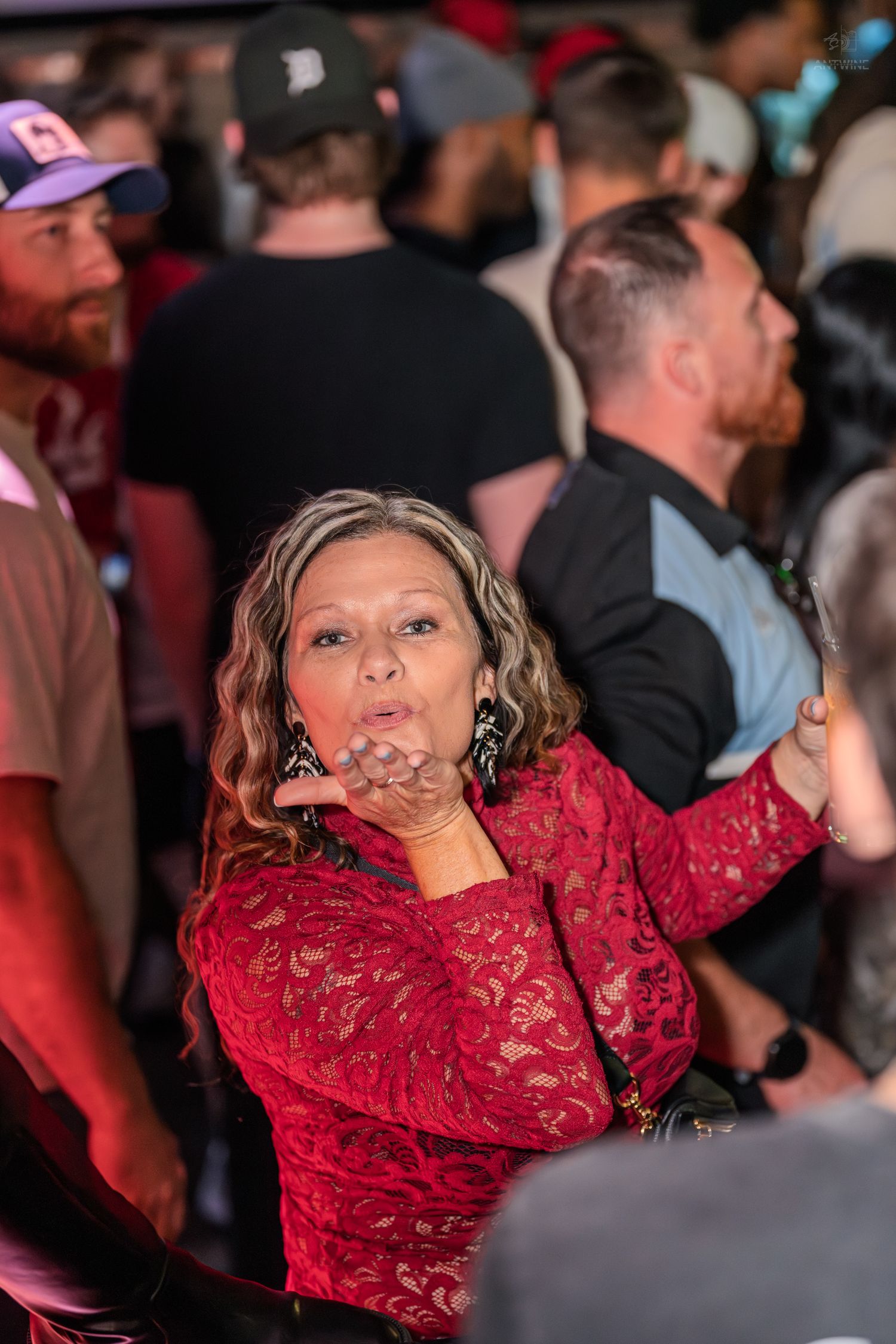 Woman in red lace dress blowing a kiss to the camera in a crowded bar.