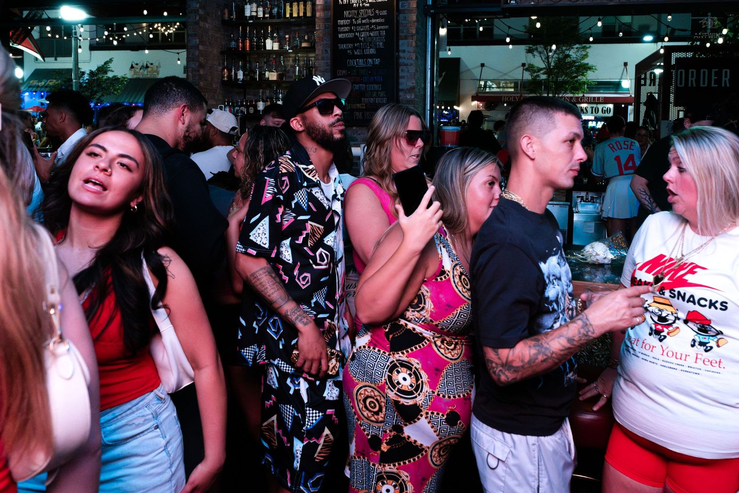 Diverse crowd enjoying a lively outdoor bar event at night in summer clothing.