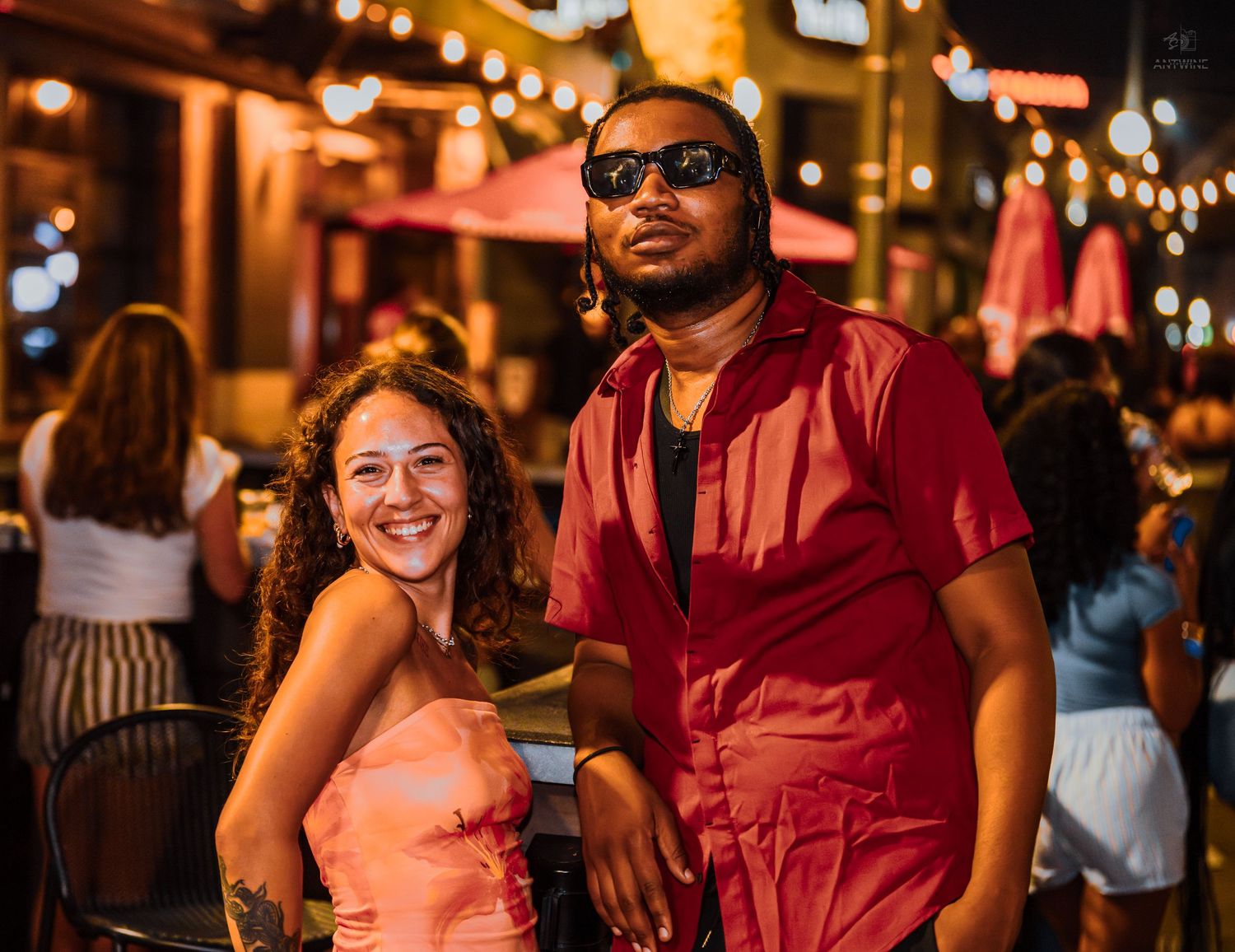 Smiling couple posing together at outdoor nighttime social gathering with string lights.
