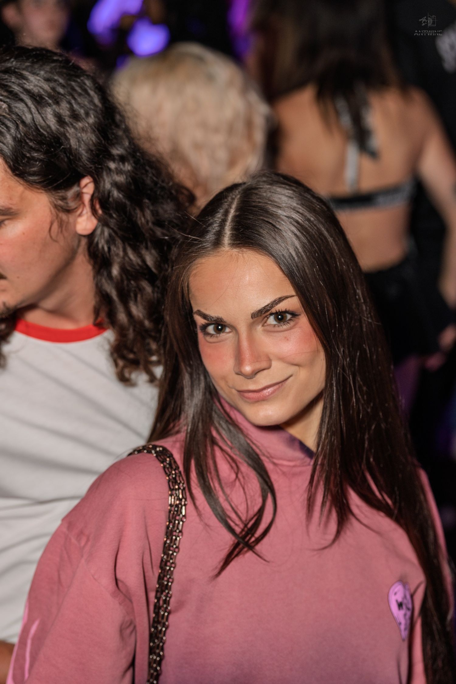 Young woman in pink sweatshirt smiling at a nightclub party event.