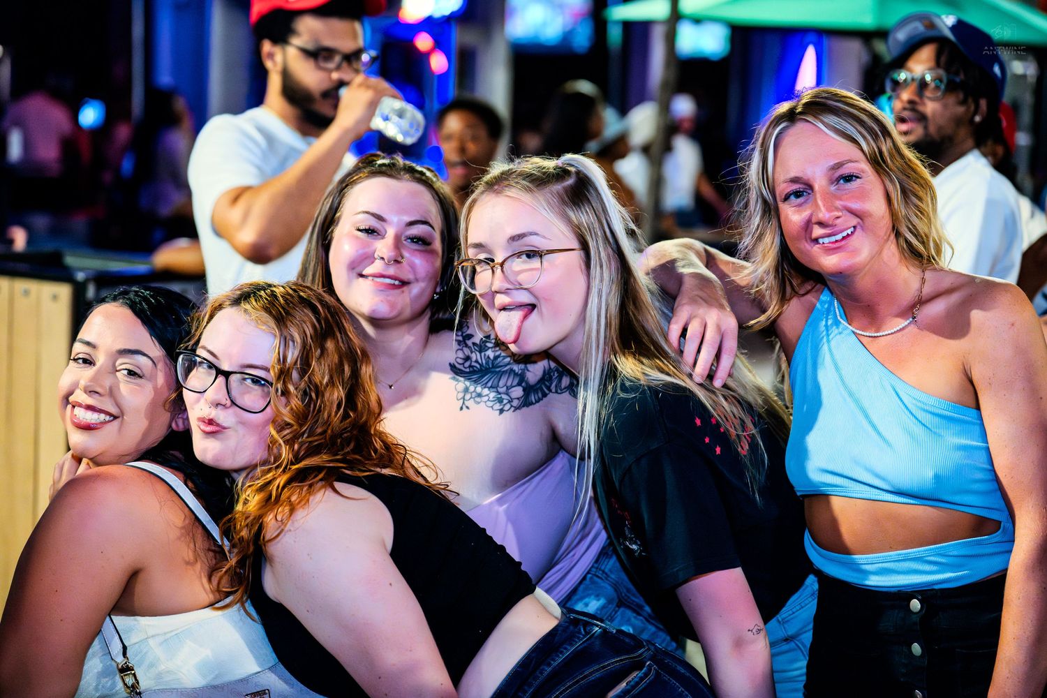 A group of five women pose and smile together at a vibrant nightclub event.