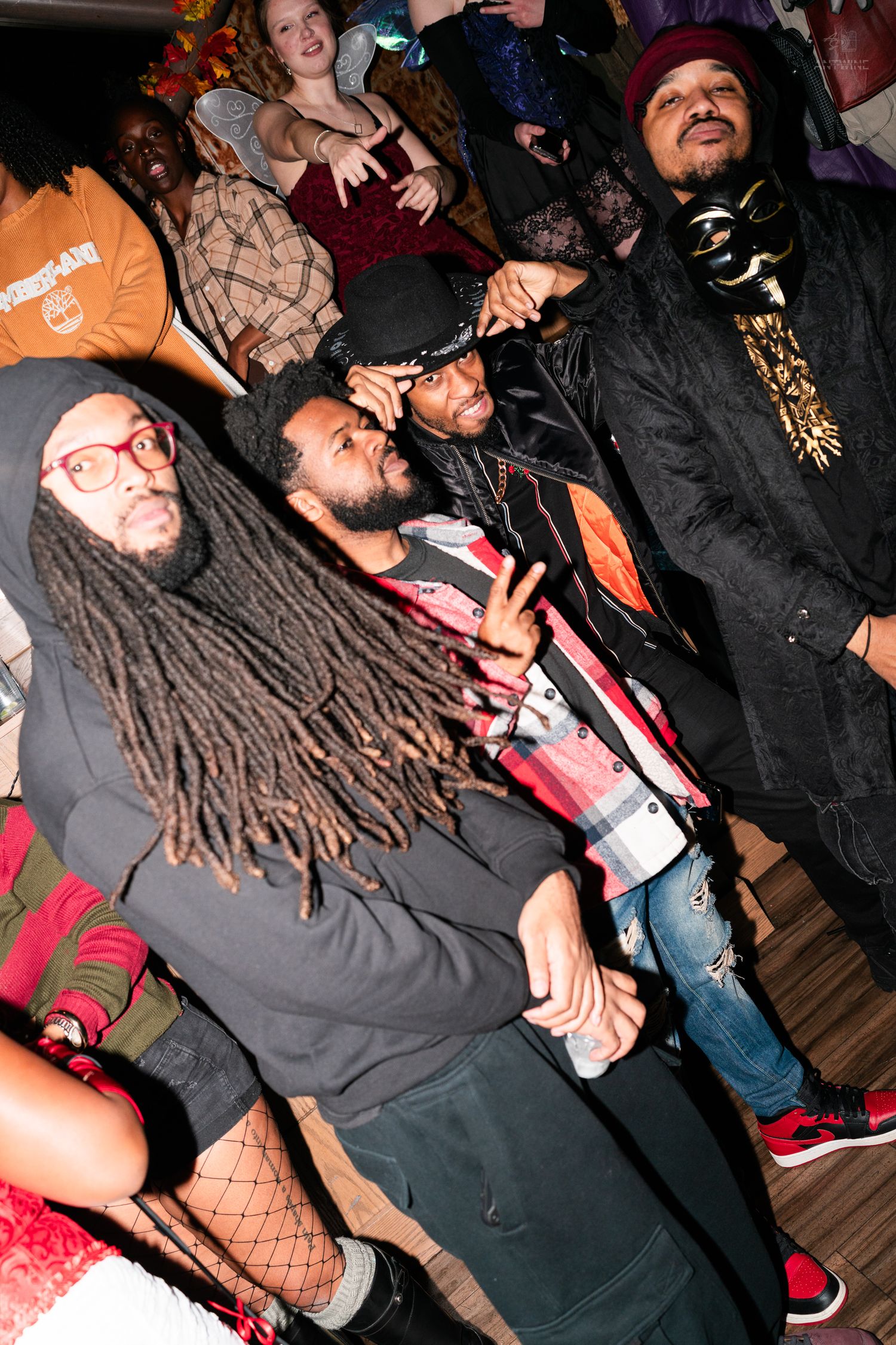 Group of men in Halloween costumes throwing peace signs at a festive nightclub event.