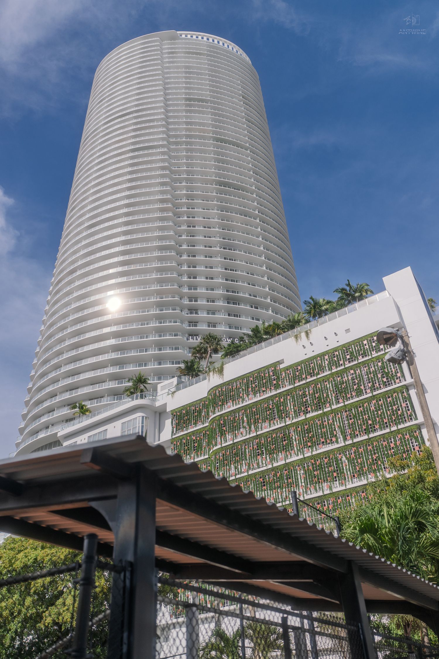 Towering modern skyscraper with curved white facade and green vertical garden wall under blue sky in Miami.