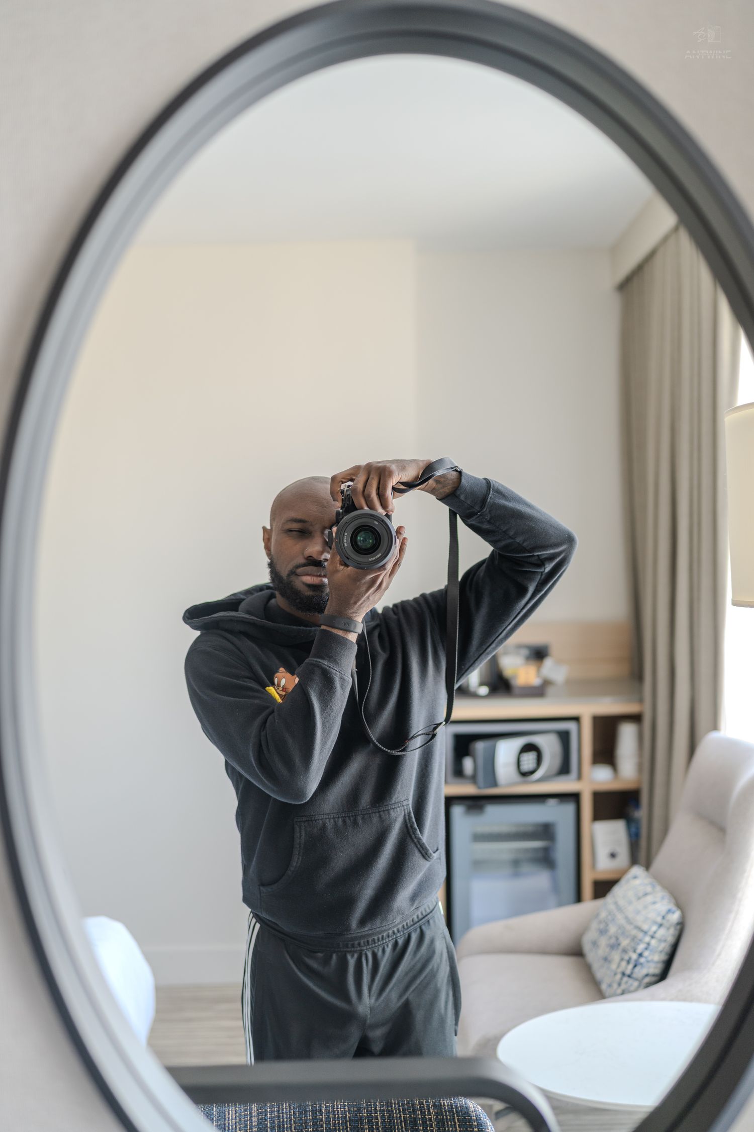 Bald man taking a mirror selfie with a DSLR camera in a modern hotel room.