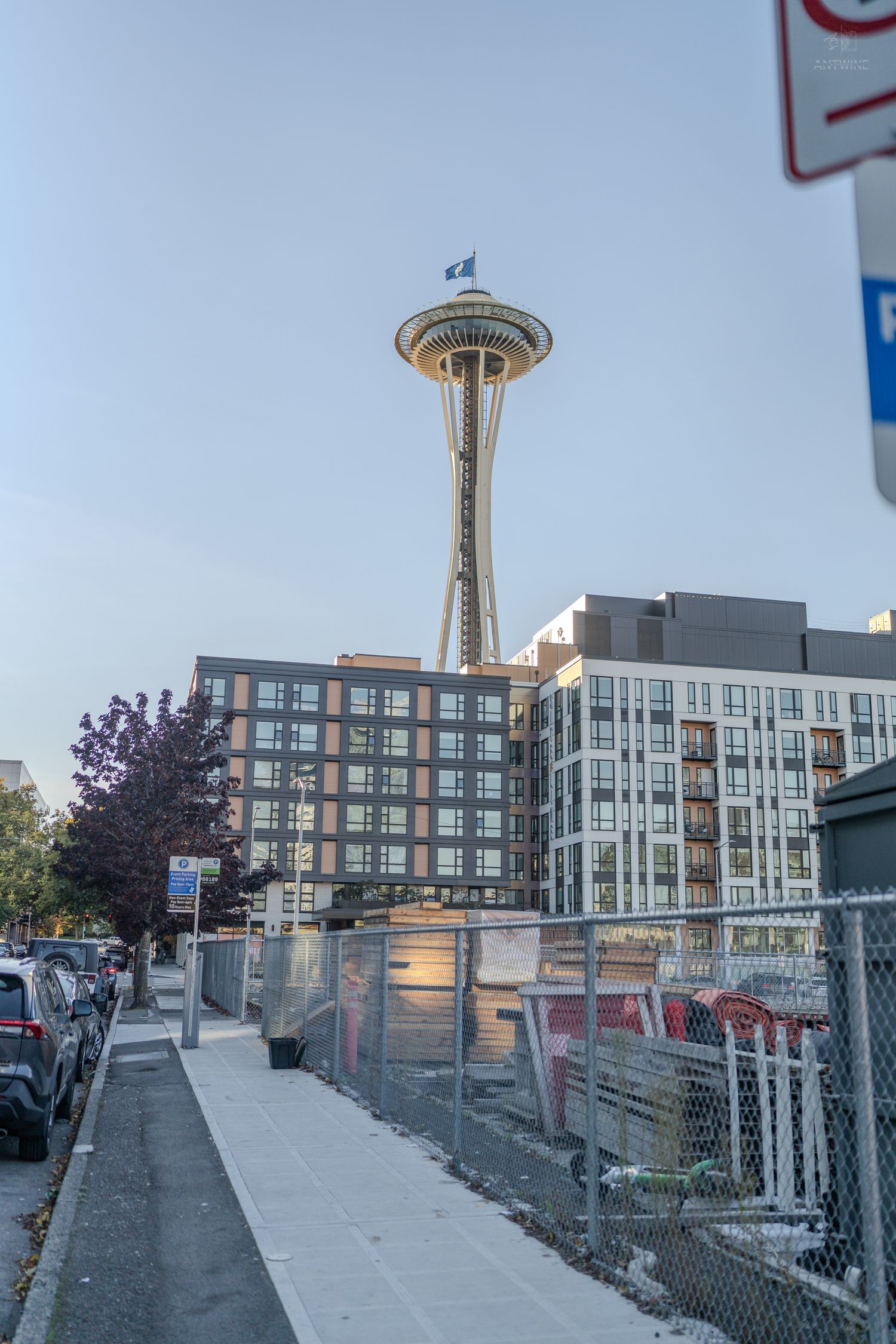 Seattle Space Needle rising above residential buildings viewed from a city sidewalk.