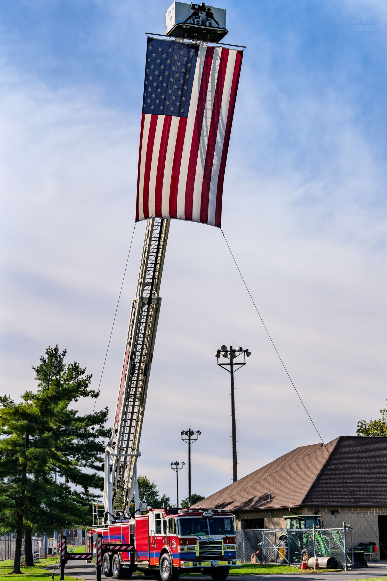 Red fire truck with extended ladder displaying a large American flag against a blue sky.