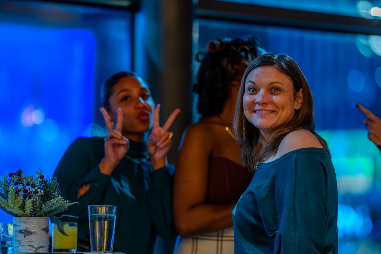 Women smiling and posing with peace signs at a social event with blue ambient lighting.