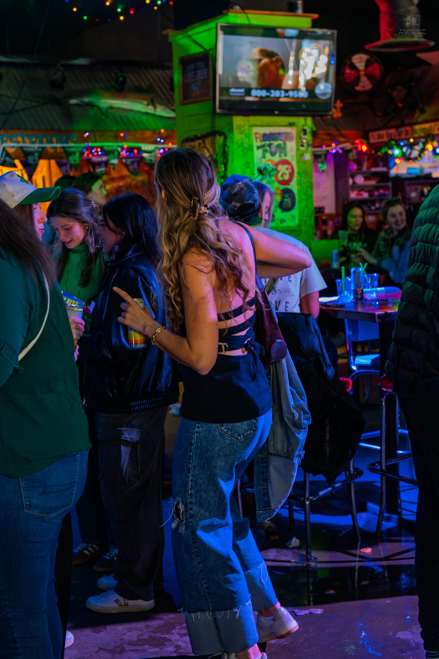 People socializing and dancing in a vibrant neon-lit bar with green lighting.