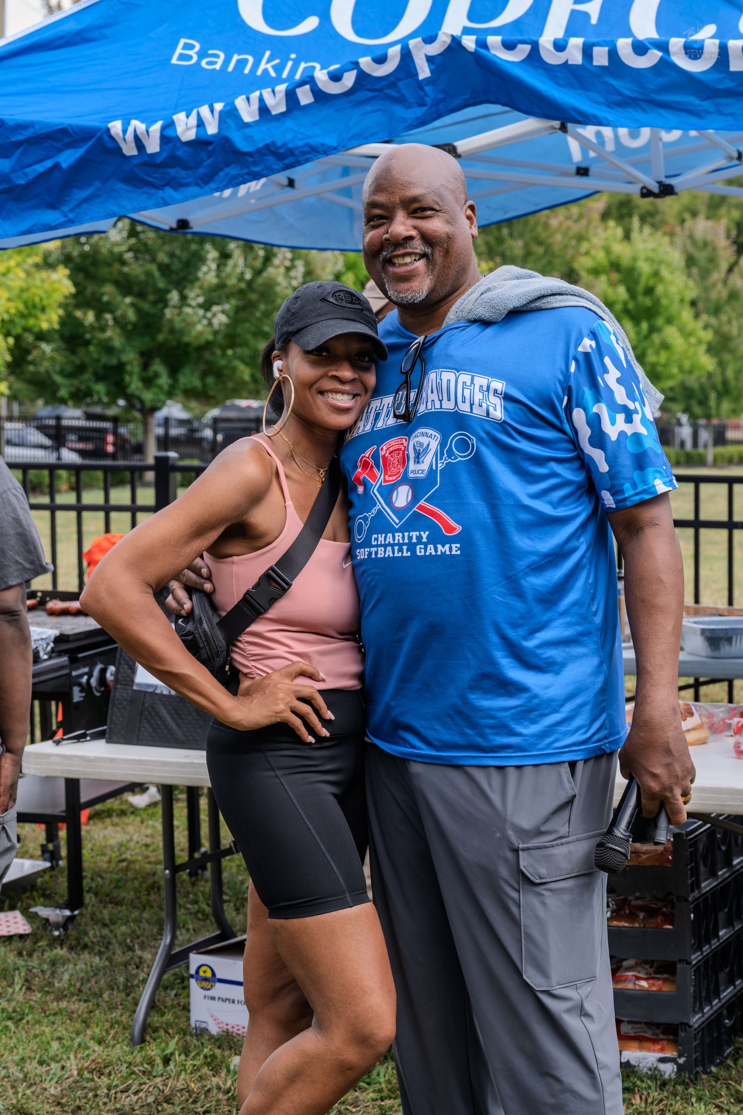 Smiling couple posing together at a Battle of the Badges Charity Softball Game outdoor event.