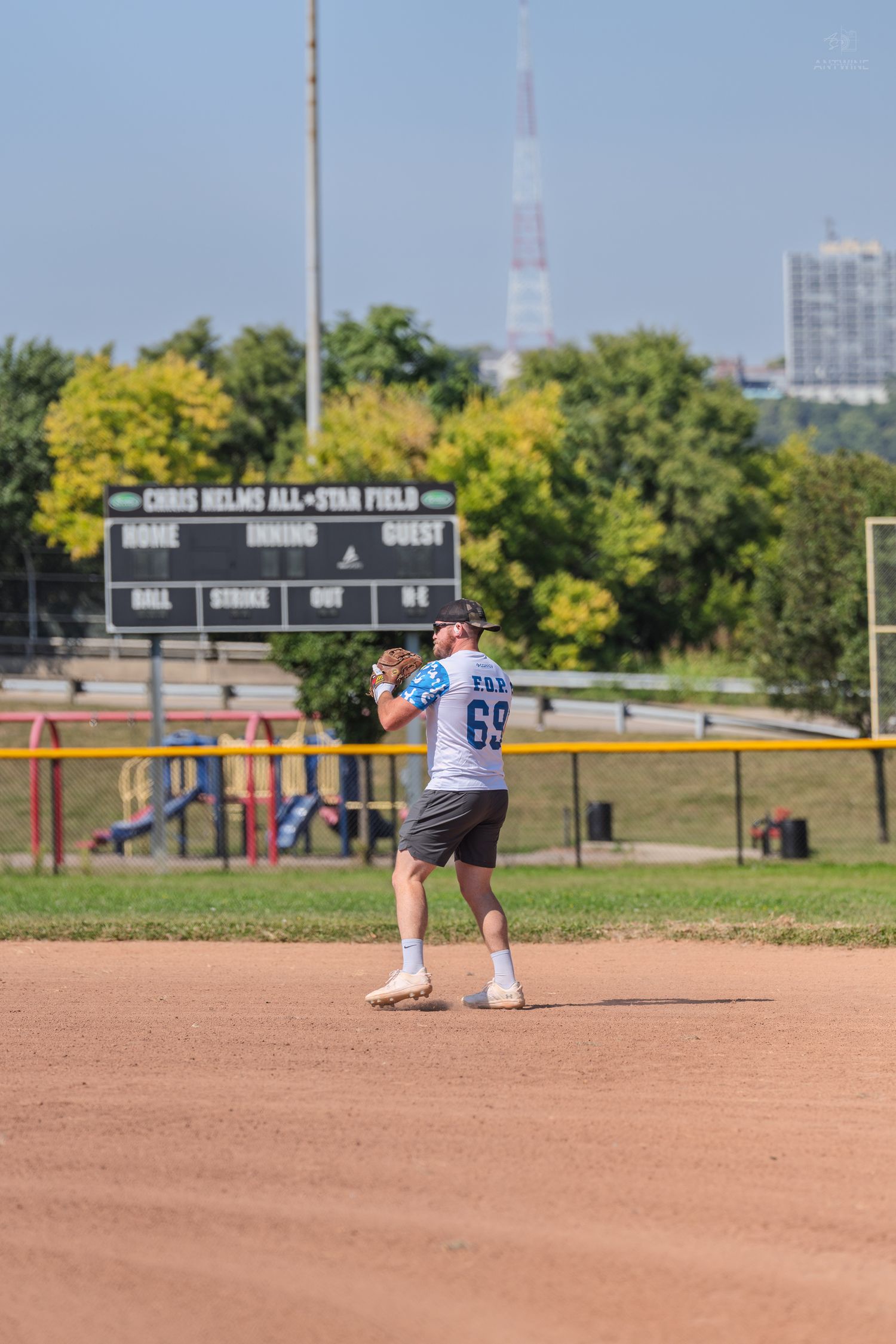 Baseball player #69 in blue jersey throwing ball on dirt infield at Chris Helms All-Star Field on sunny day.