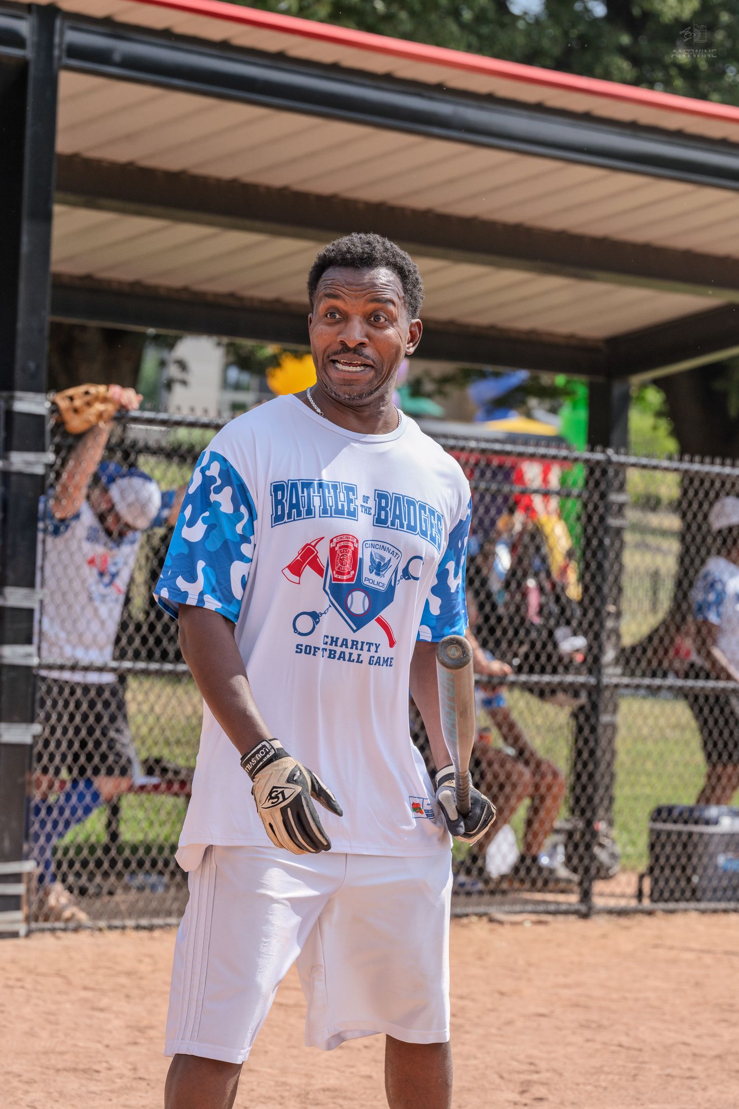 A man in a Battle of the Badges charity softball jersey smiles while wearing batting gloves.