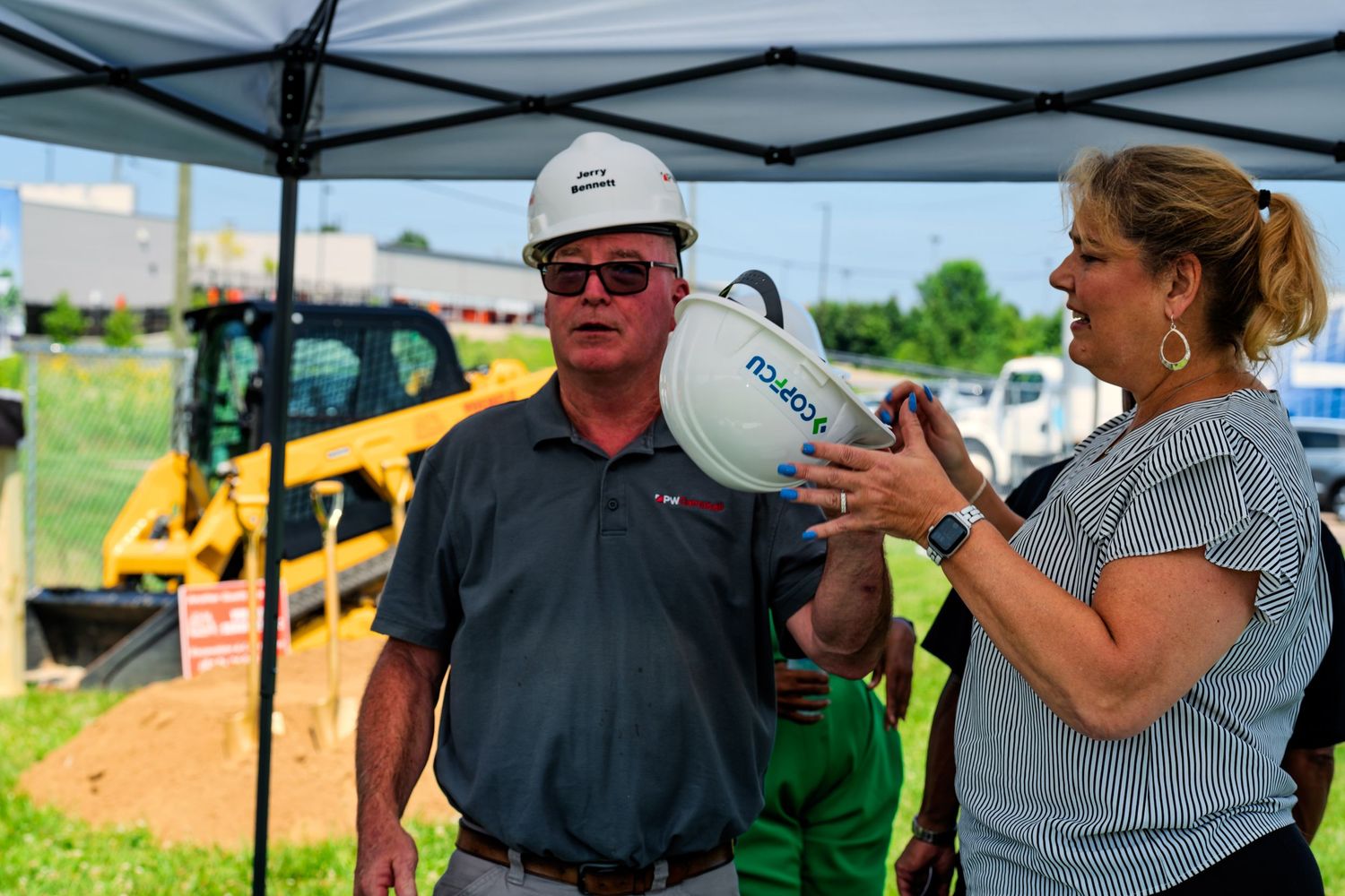 Man and woman in hard hats conversing under tent canopy at COPCU Hamilton groundbreaking ceremony.