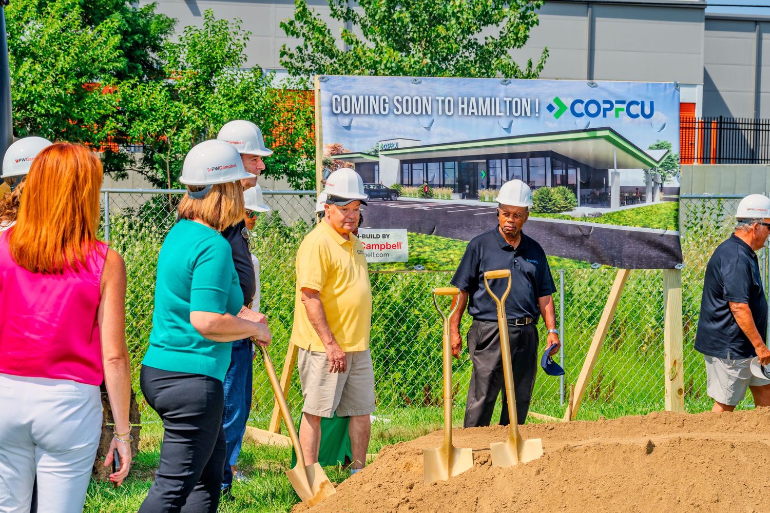 Group of people in hard hats holding golden shovels at COPFCU groundbreaking ceremony in Hamilton.