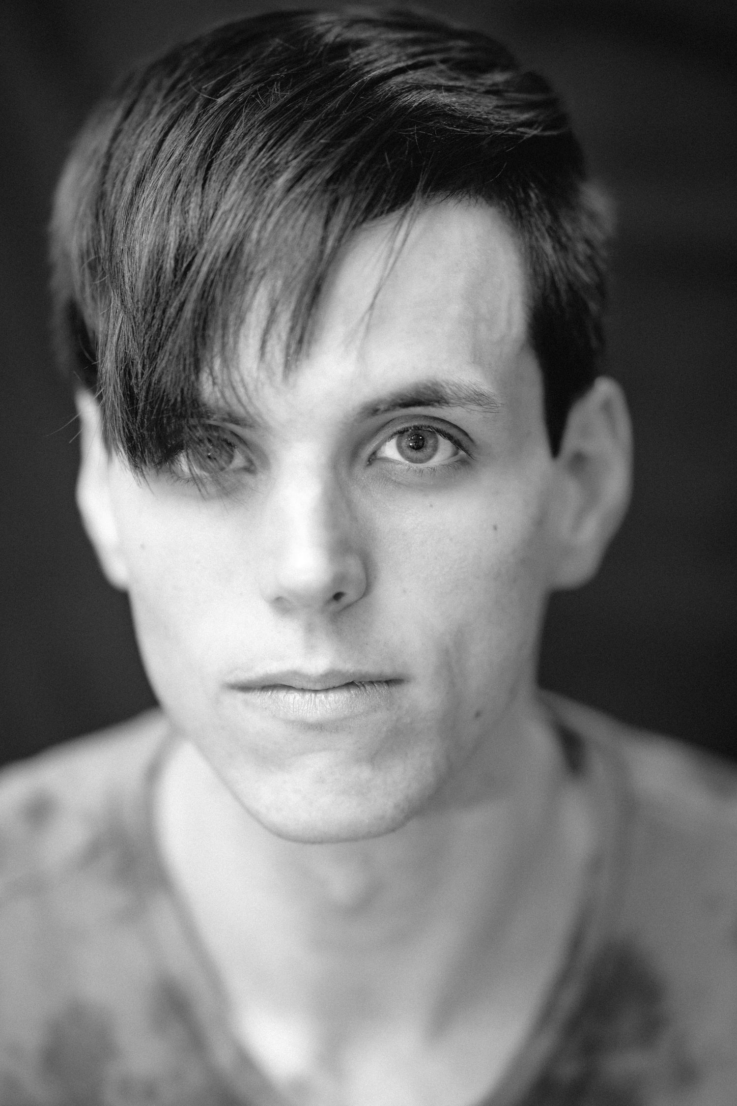 Black and white headshot of young man with side-swept dark hair and neutral expression.