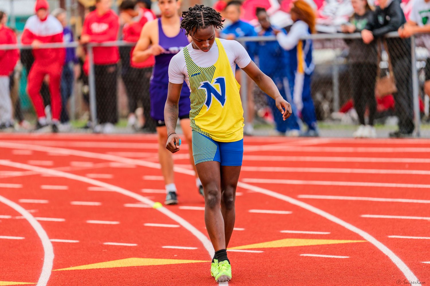 Young male sprinter in yellow and blue uniform races on red track.