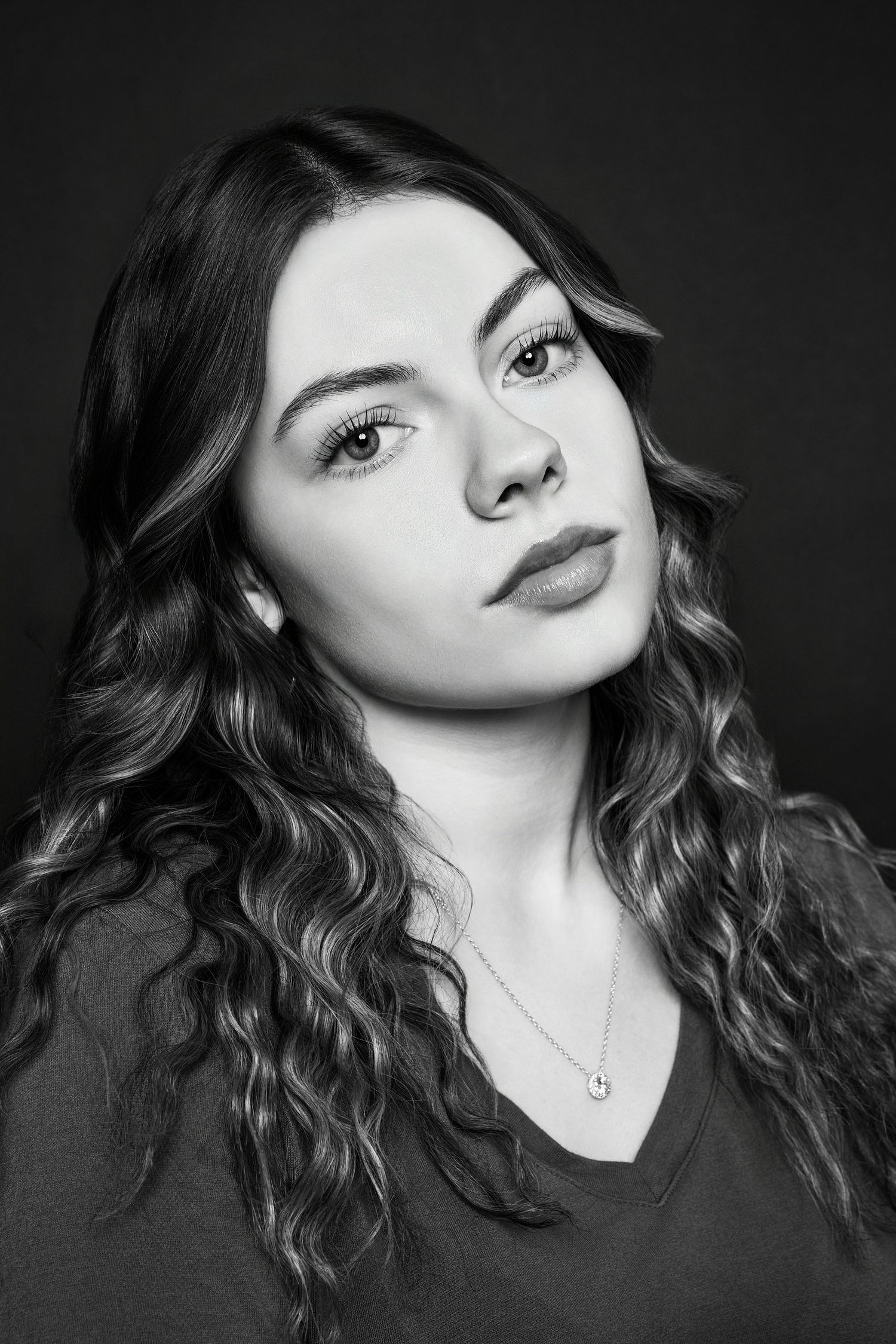 Moody black and white portrait of a young woman with curly hair and a subtle necklace.