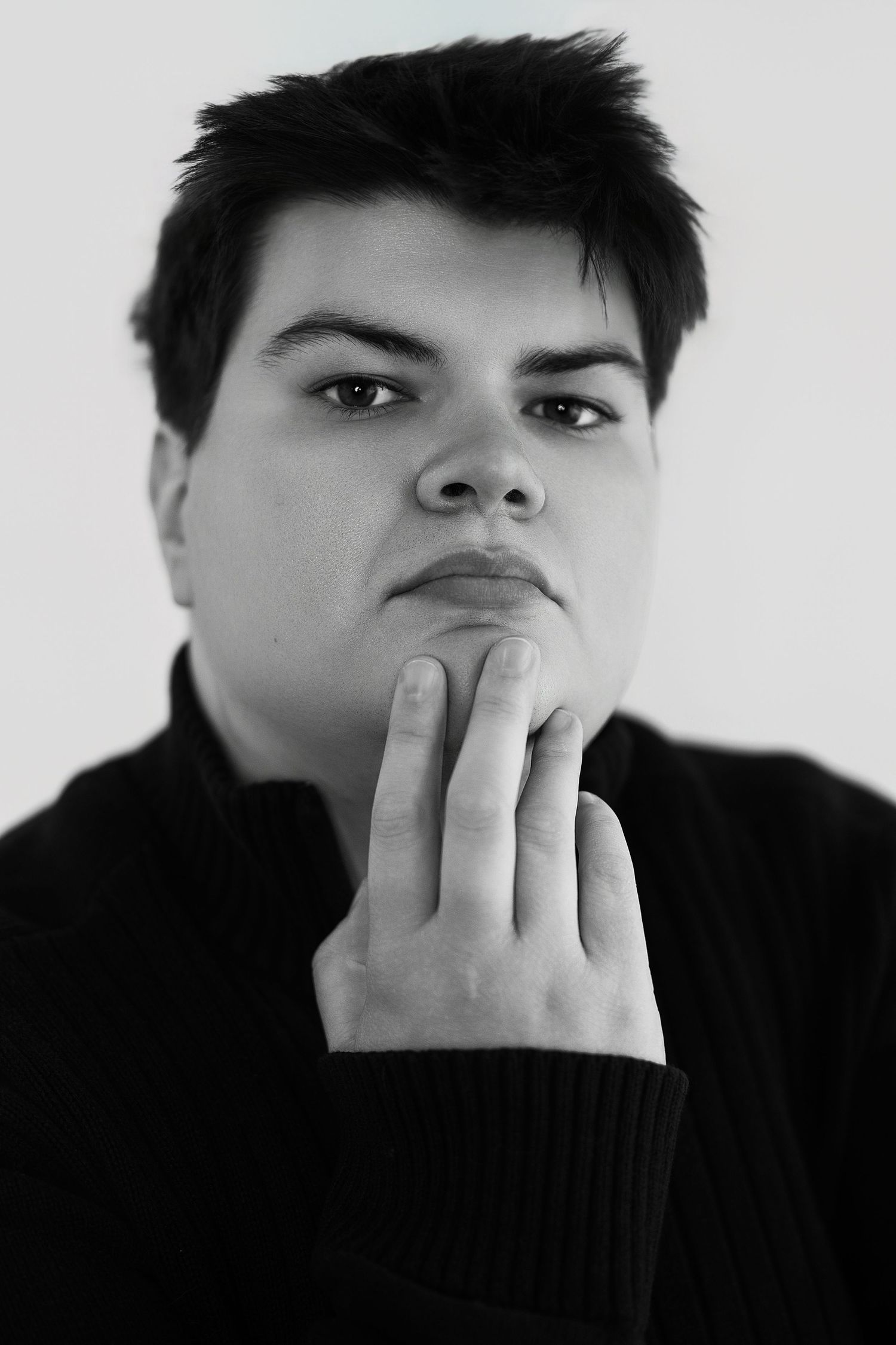 Black and white portrait of a young person in black sweater with hand raised to chin thoughtfully.