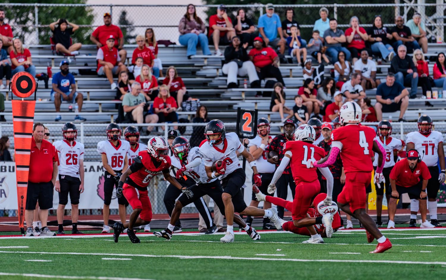 High school football players in red and white uniforms compete during an intense game with fans watching from the stands.