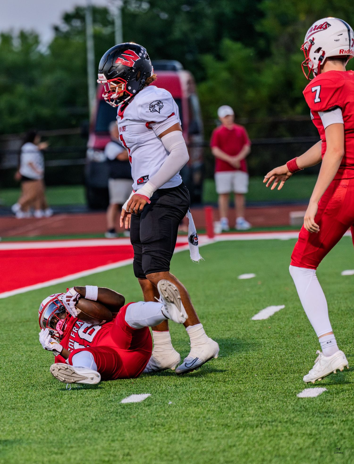 White-uniformed Firebirds football player stands over a tackled red-uniformed opponent near the end zone.
