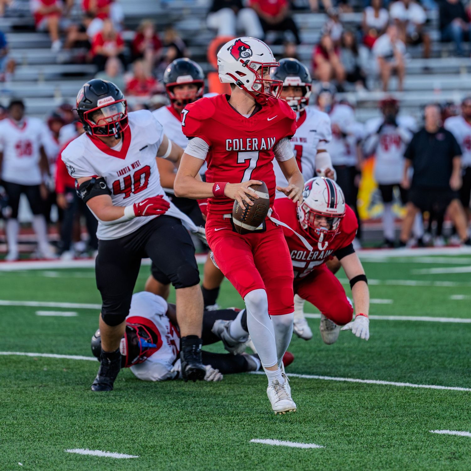 Colerain quarterback scrambles out of pocket in red uniform during a competitive high school football game.
