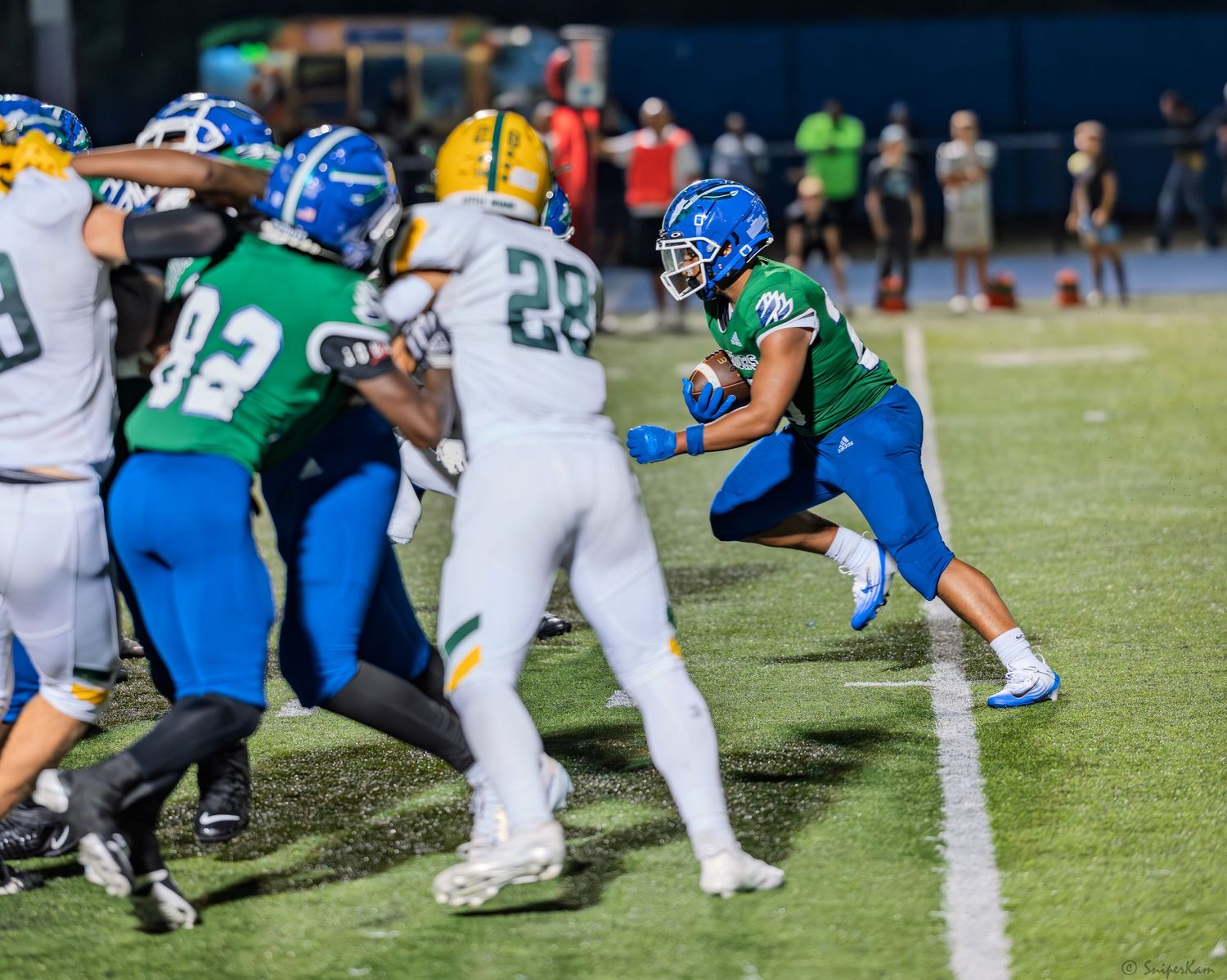Warriors football player in green and blue uniform runs around end during night game.