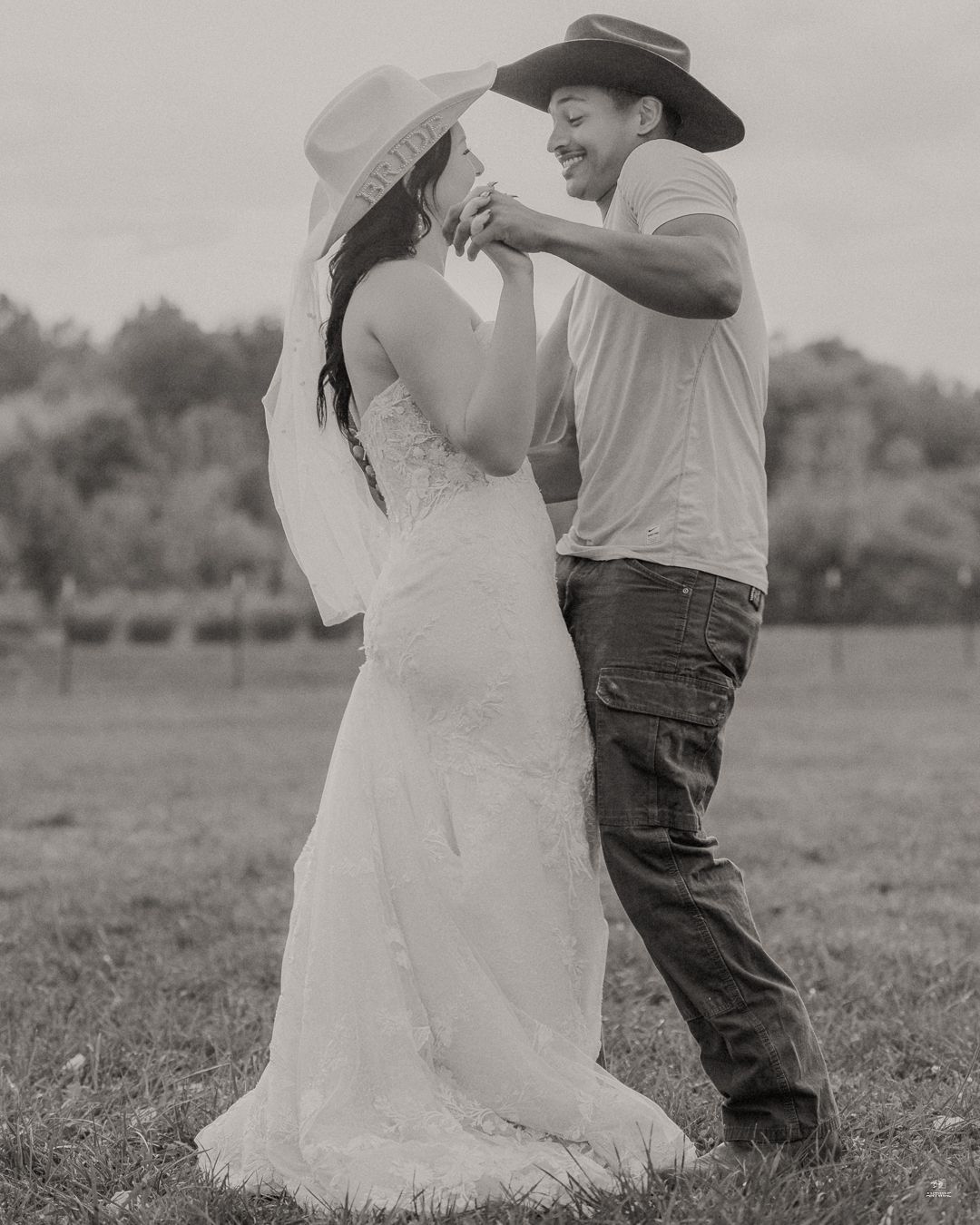 Black and white photo of bride and groom dancing in a field at their rustic outdoor wedding.