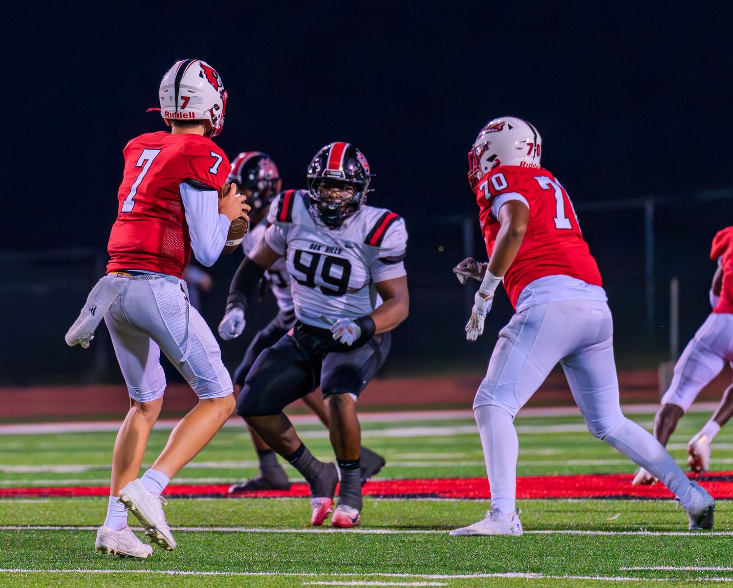 Colerain quarterback number 7 scrambles under pressure from a defensive lineman during a night game.